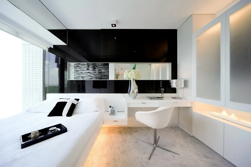 A modern minimalist bedroom featuring a floating white bed and desk set against a reflective high-gloss black wall panel with a built-in horizontal mirror.