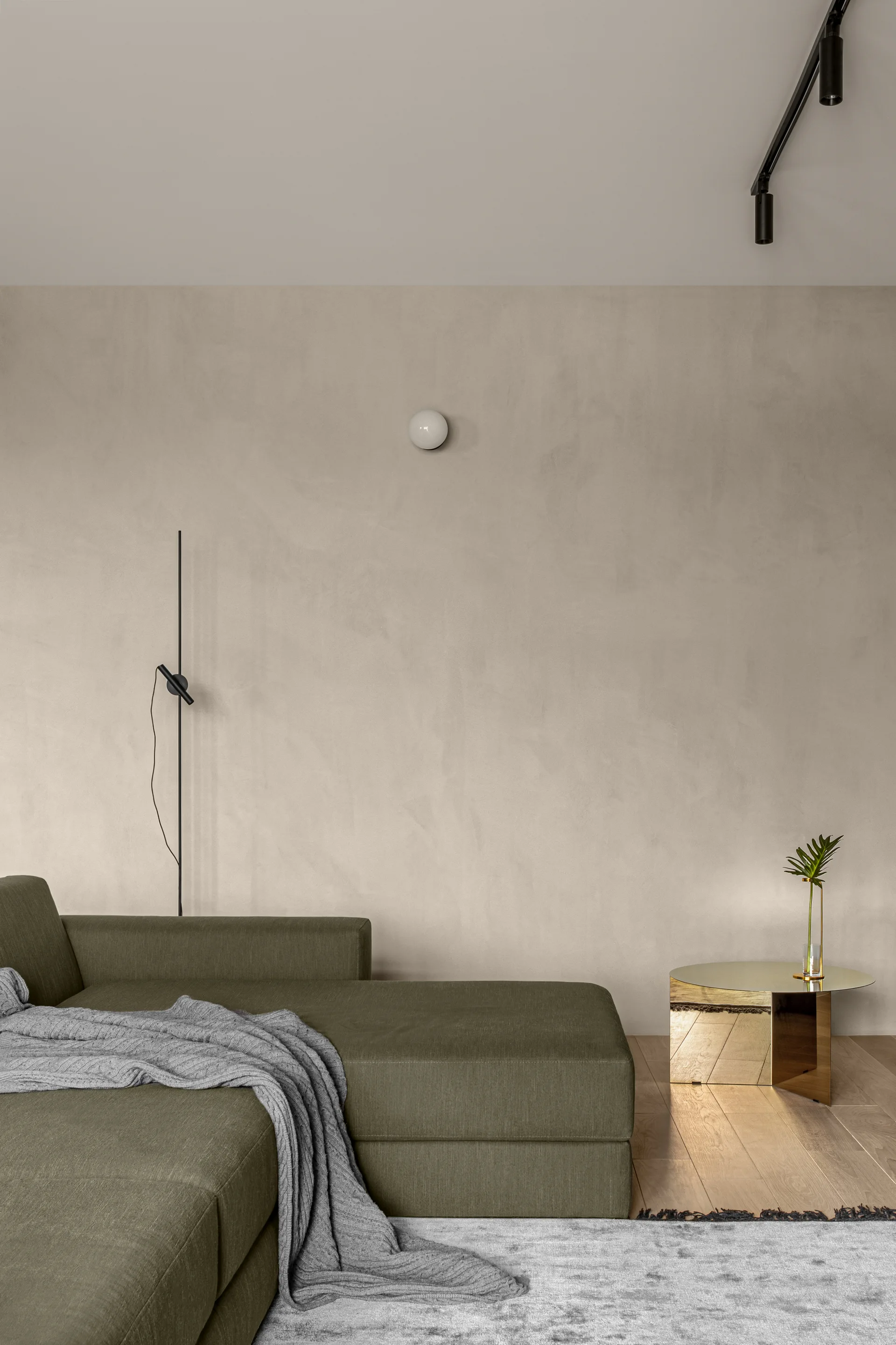 An olive green sectional sofa with a gray throw blanket sits against a beige plaster wall near a mirrored gold side table.