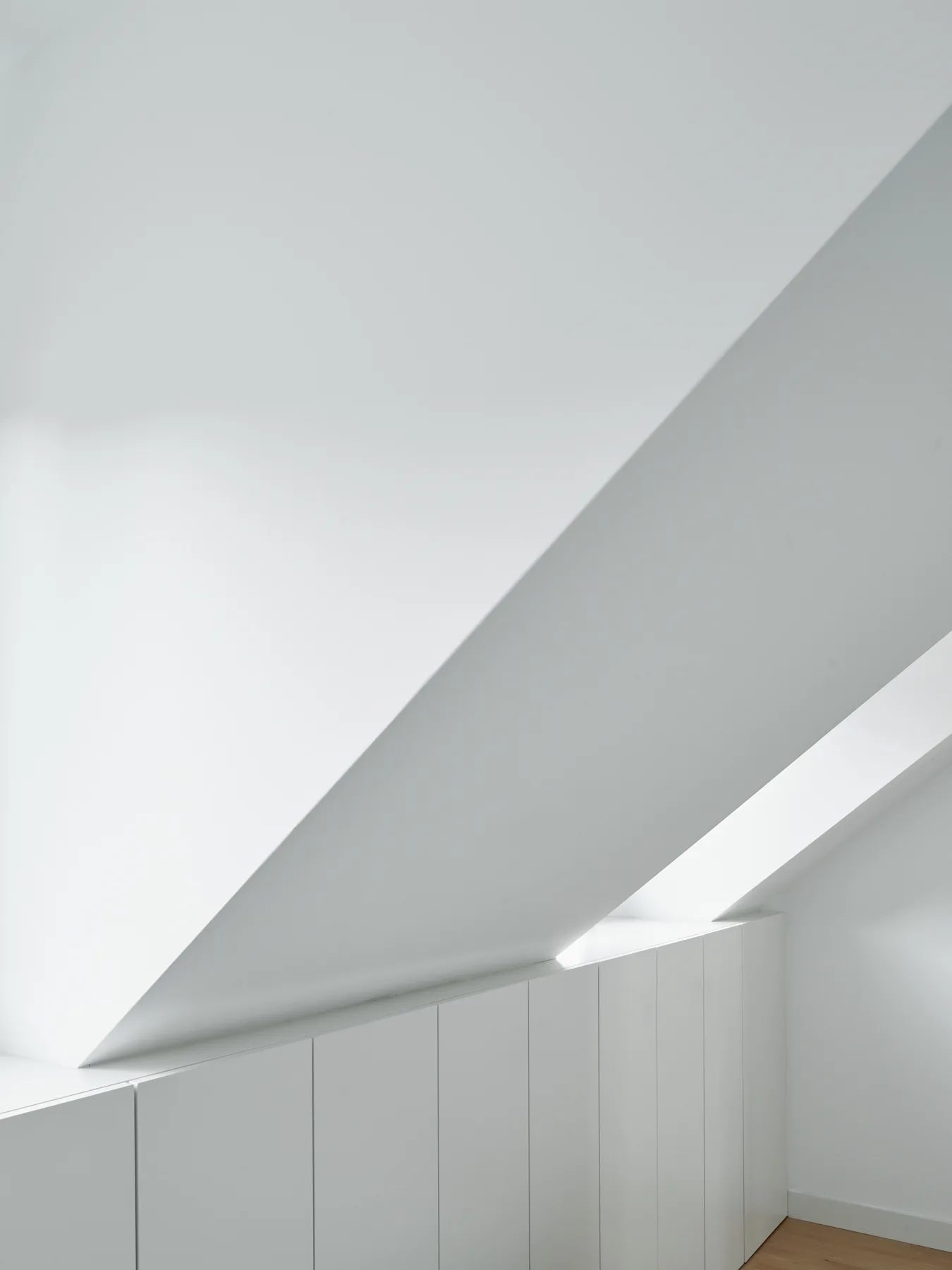 White built-in knee wall cabinetry sits under a sharply sloped attic ceiling on a light wood floor.