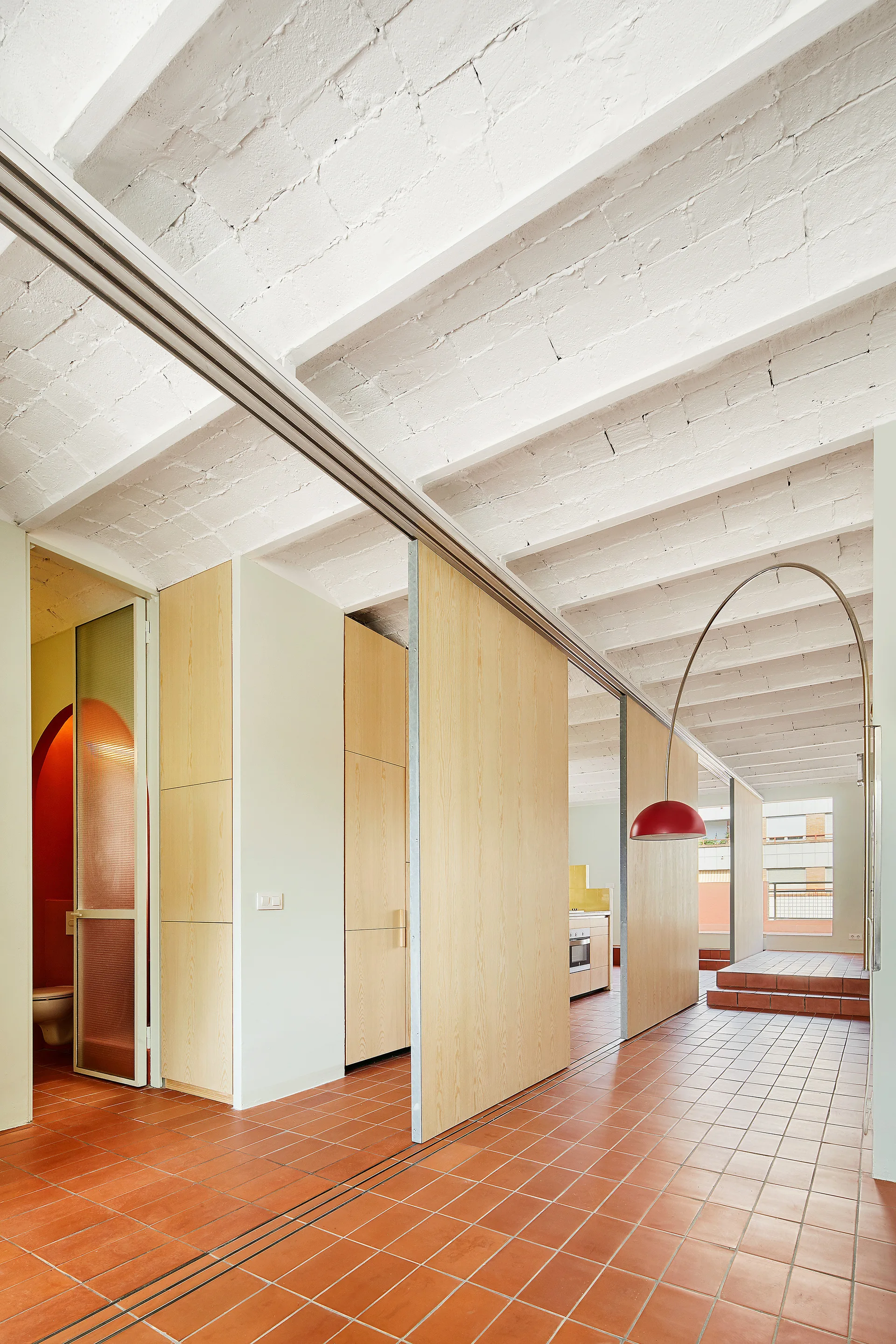 An open interior space with terracotta floor tiles, light wood sliding partition walls, and a white painted brick ceiling.