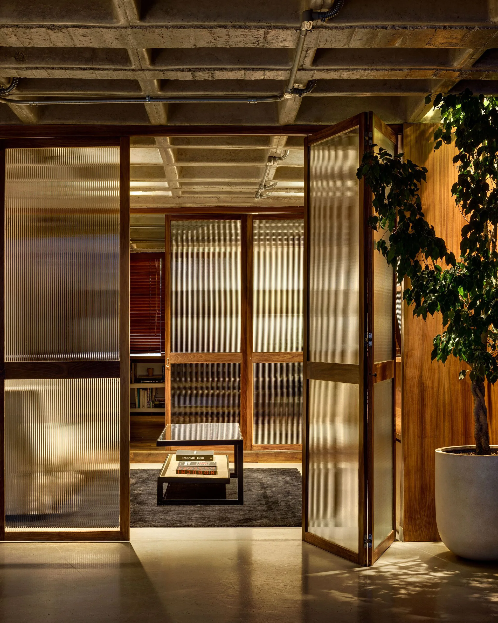 Warm wood-framed fluted glass folding doors beneath an exposed concrete waffle ceiling in a contemporary interior.