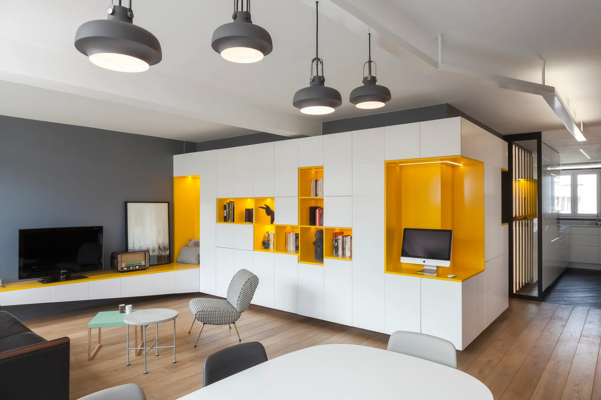 A modern living room features a large white built-in storage unit with bright yellow open shelving niches, a grey accent wall, and wood flooring.