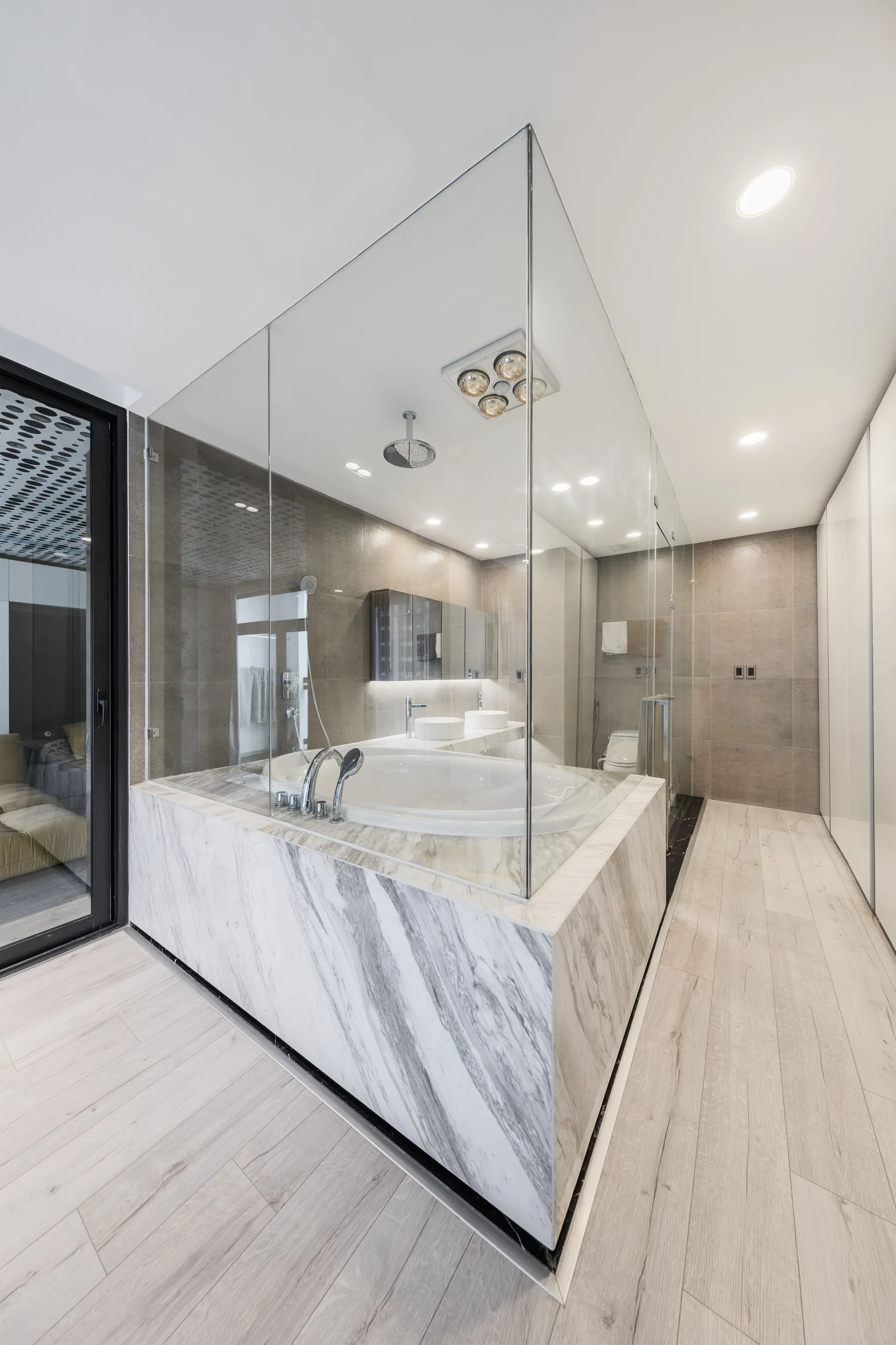 A modern bathroom featuring a circular soaking tub inside a glass-enclosed wet room with a prominent marble platform and wood-look floor tiles.