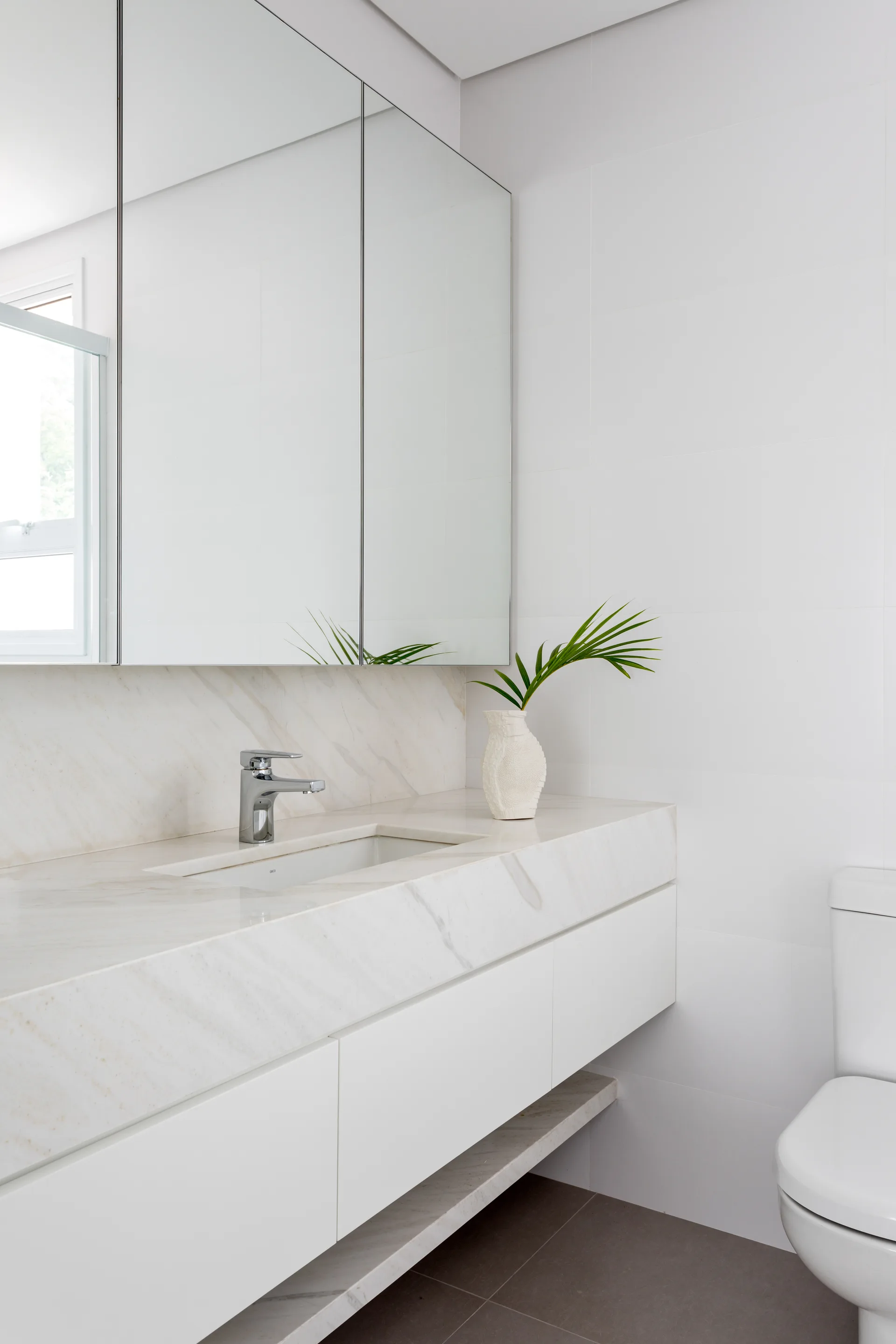 A modern bathroom features a floating white vanity with a veined stone countertop, integrated sink, and a large mirrored cabinet.