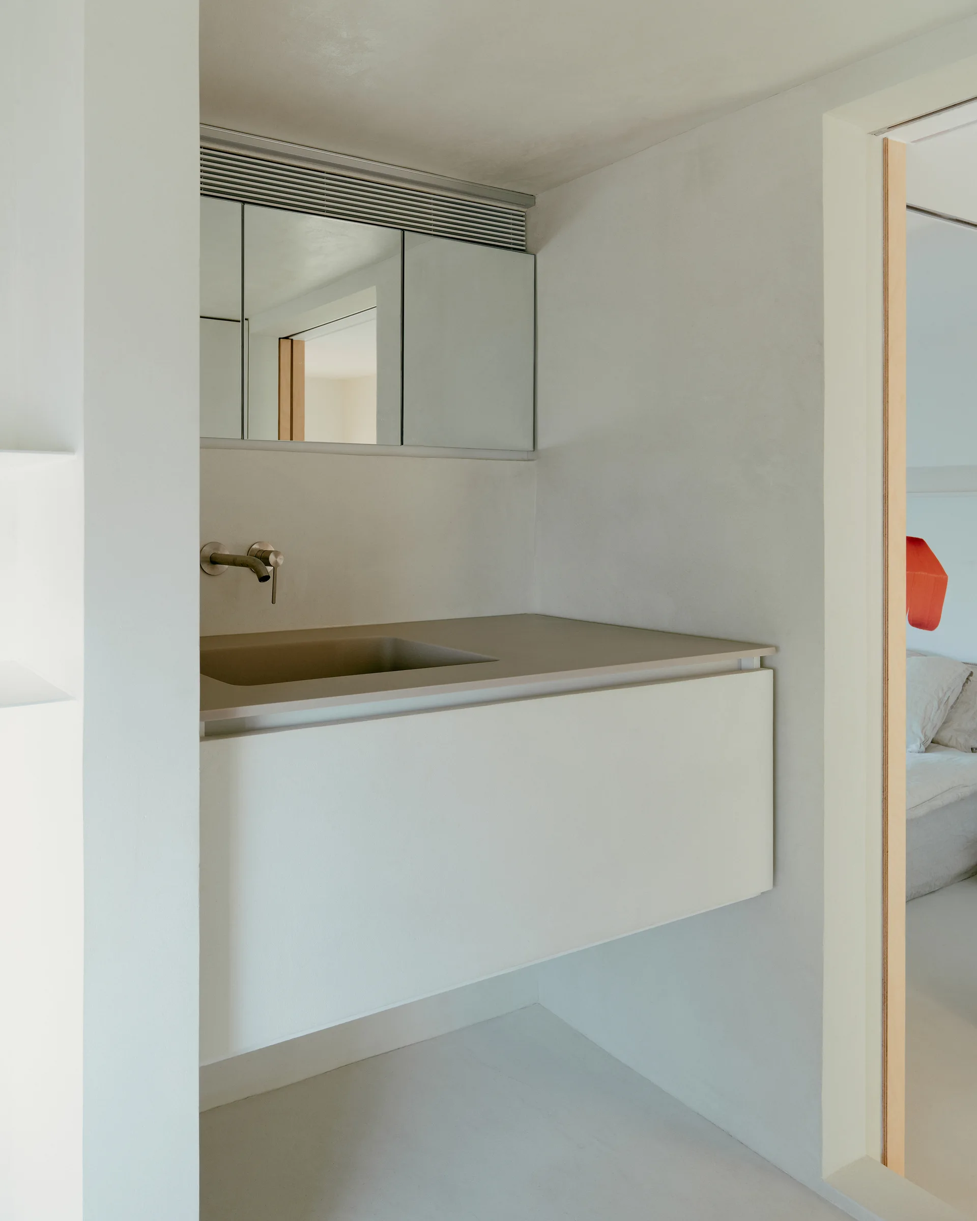 A minimalist floating vanity with an integrated sink and wall-mounted faucet set against light grey plastered walls.