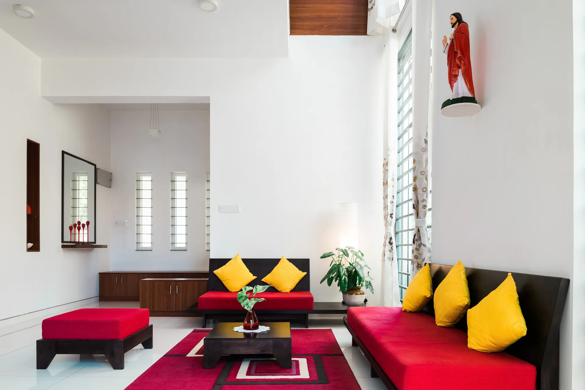 A living room features low-profile red sofas with yellow pillows, a dark wood coffee table, and a geometric red rug on glossy white tile floors.