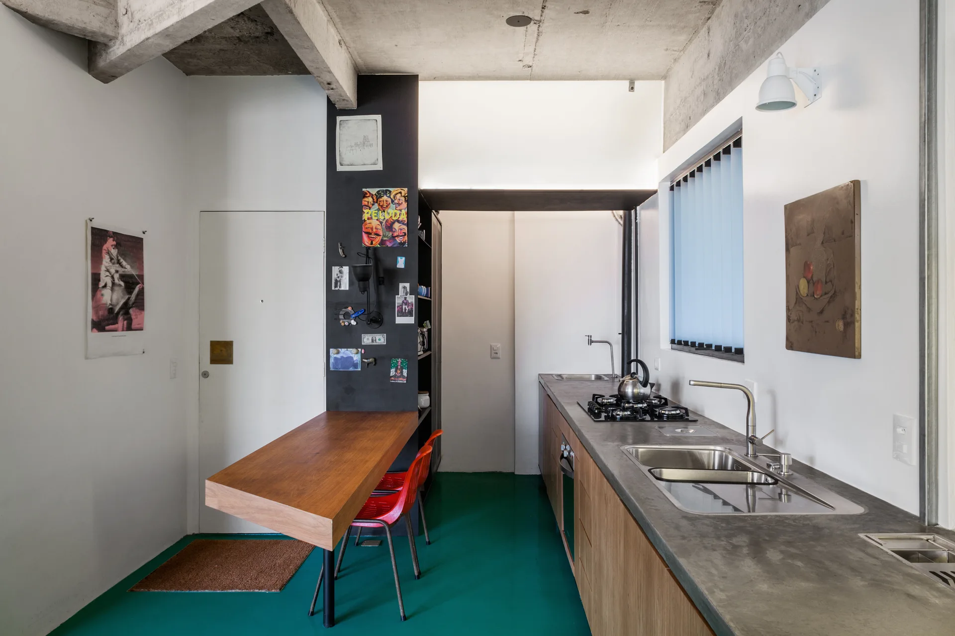 A narrow kitchen features a bright green floor, a concrete countertop with integrated sink, and a cantilevered wood table against a black accent pillar.
