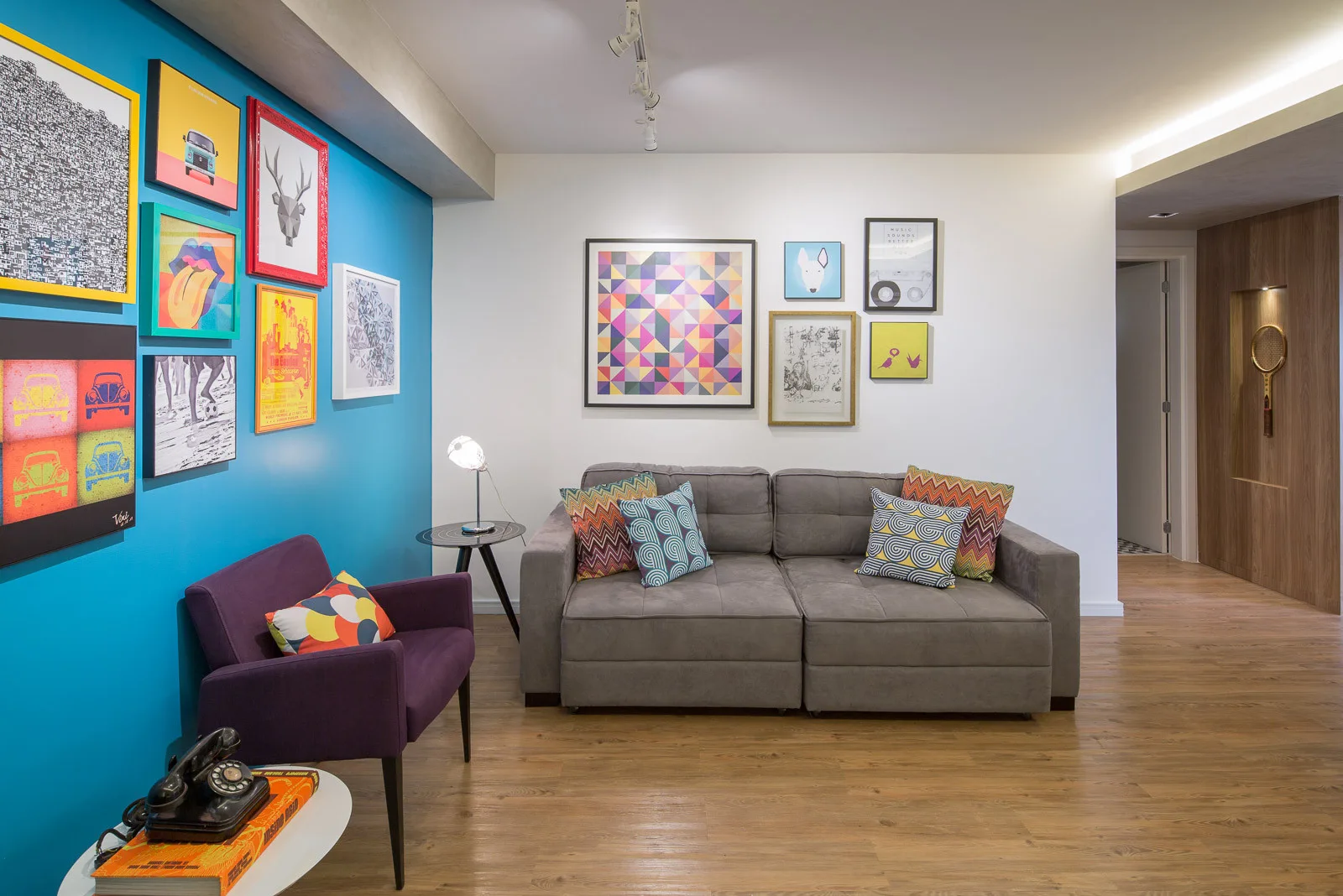 A modern living room featuring a grey sofa and a purple armchair set against a blue accent wall with framed art.