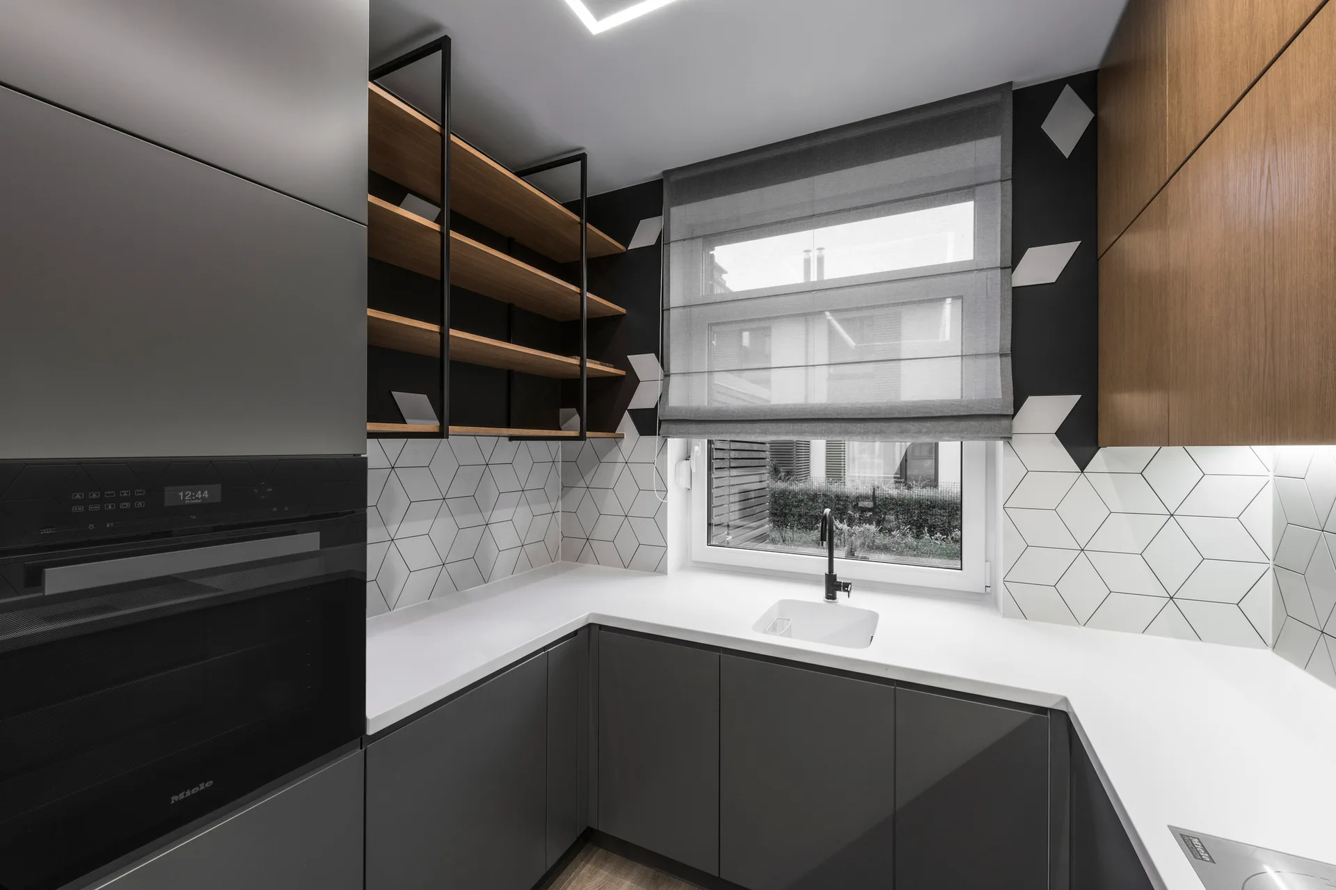 A modern kitchen corner featuring dark grey flat-panel cabinets, a white countertop, hexagonal tile backsplash, and open wood shelving.