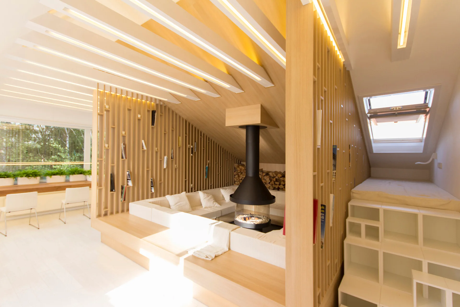 A modern attic living room features a suspended black fireplace, a built-in white sectional sofa, and a vertical wood slat partition under a sloped ceiling.