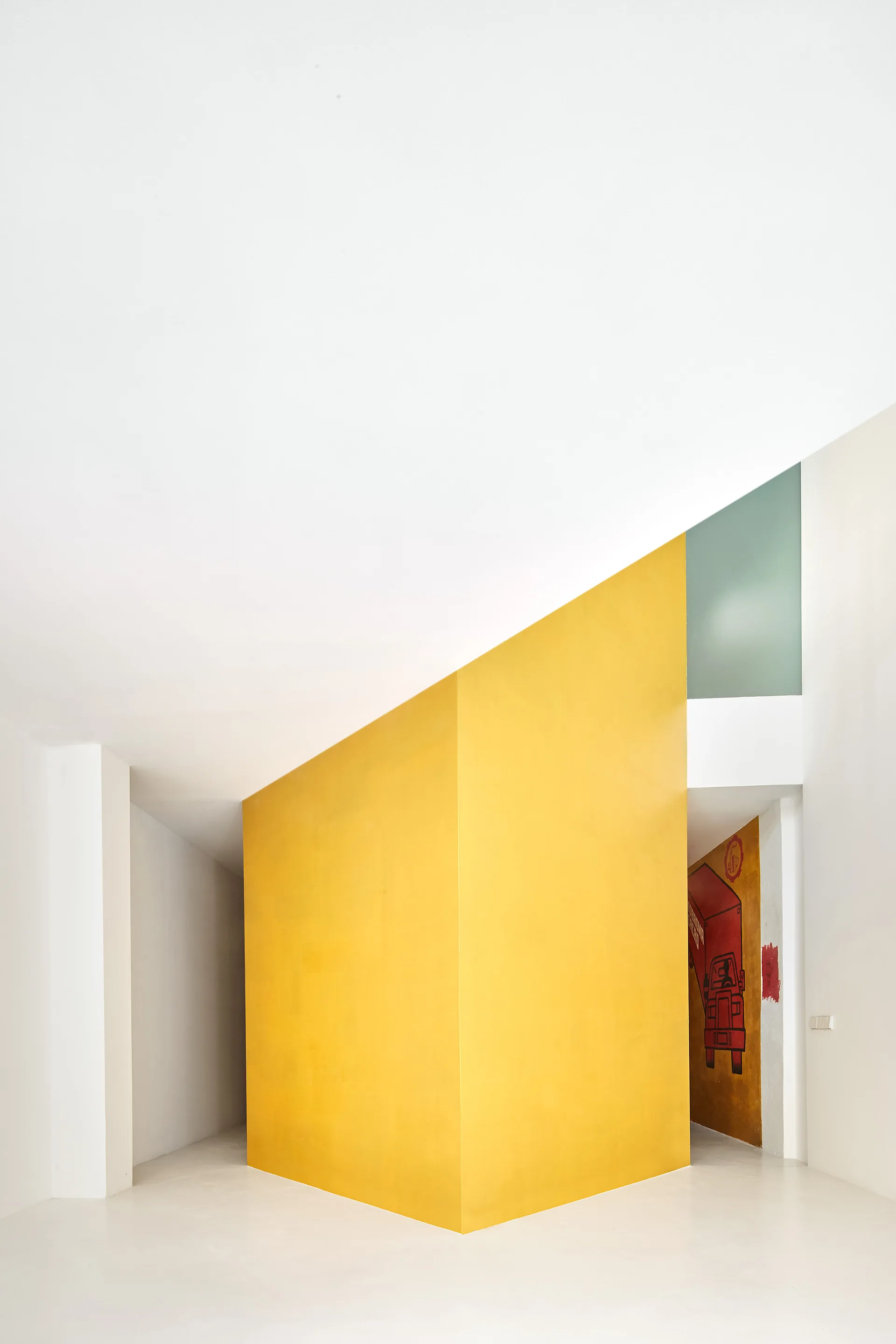 A minimalist white hallway featuring a large, angular matte yellow partition wall and smooth light-colored floors.