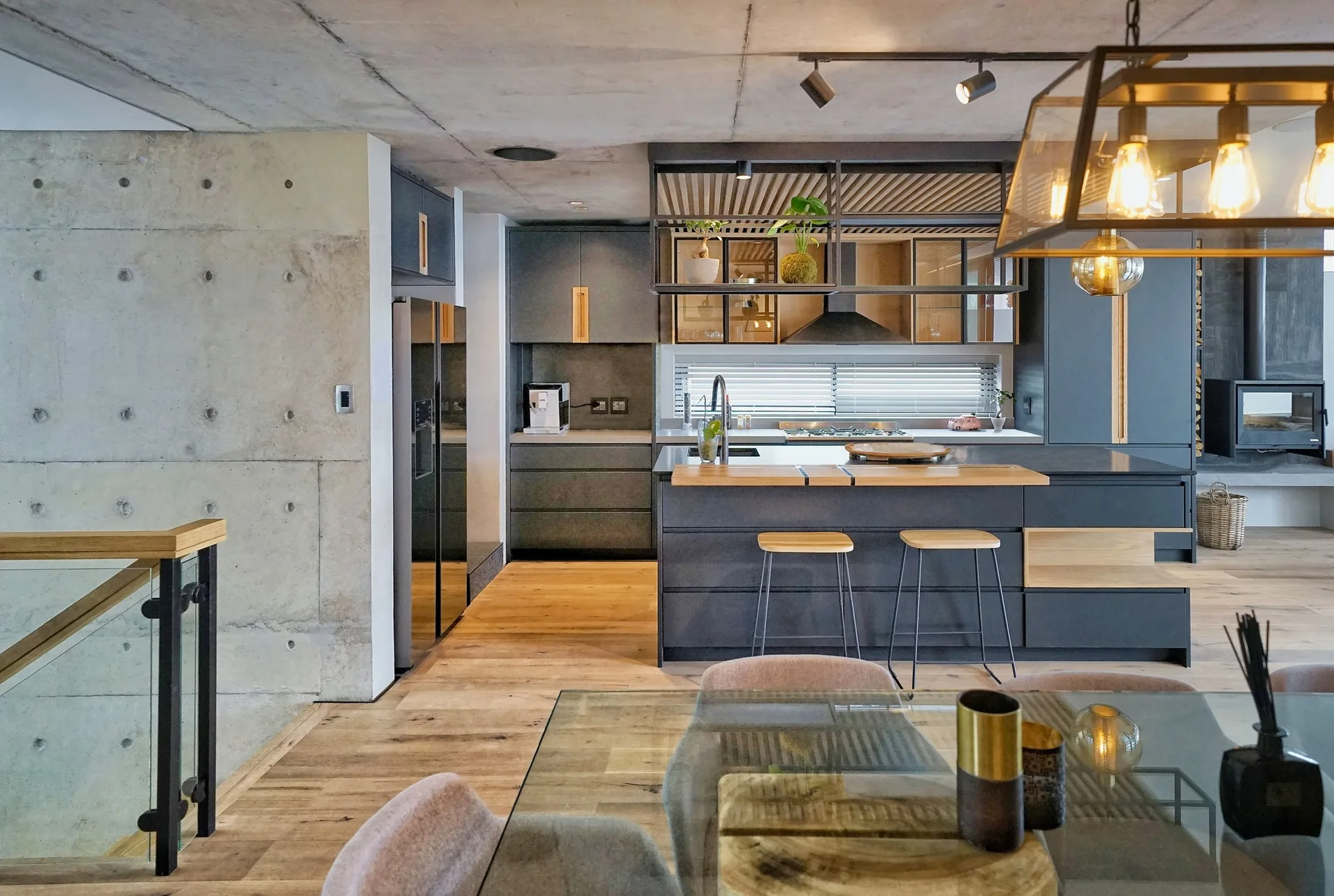 A modern kitchen featuring dark grey cabinets, a raw concrete ceiling, and a dark island with wood stools.