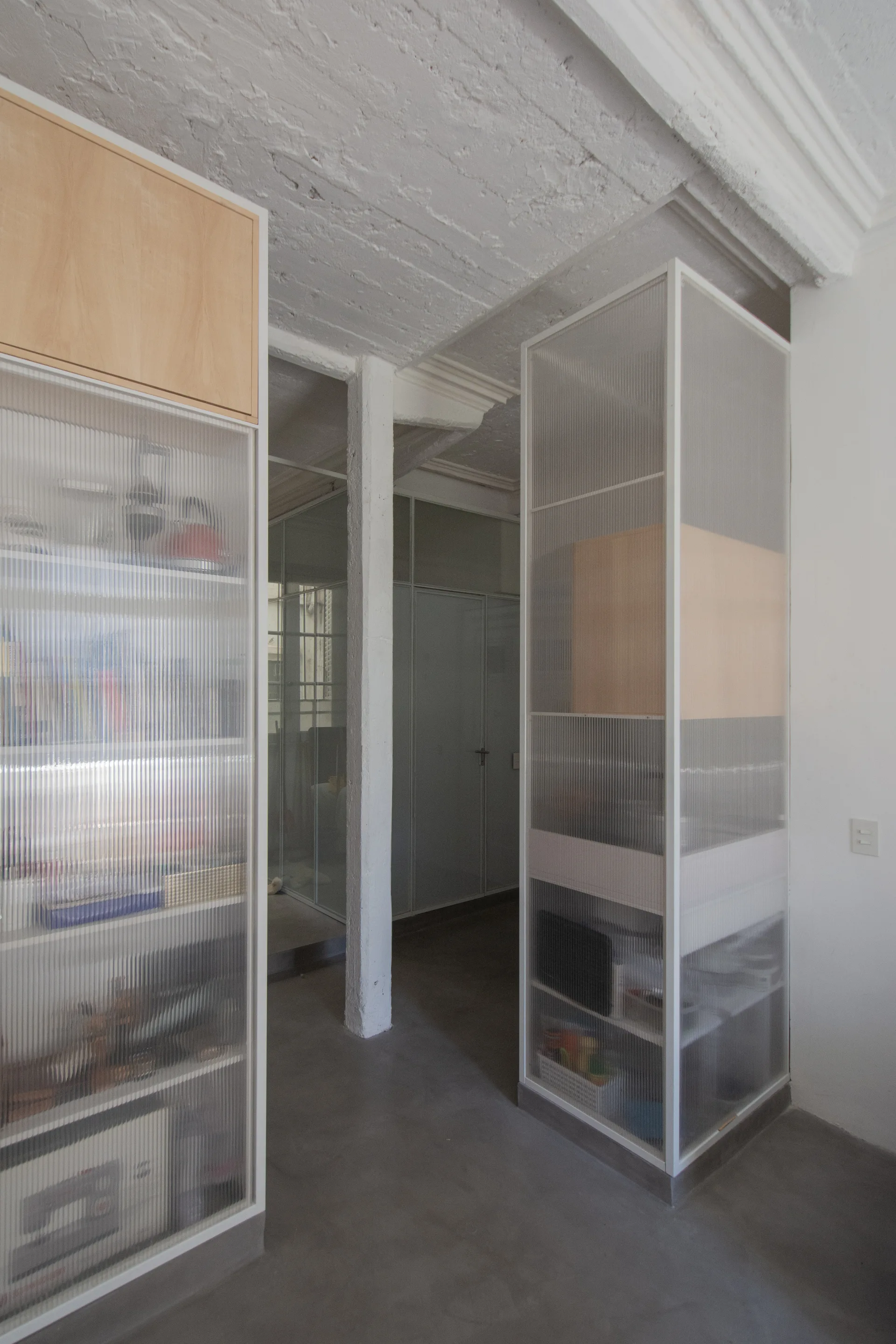 Two tall white cabinets with fluted glass doors and light wood inserts stand on a concrete floor in an industrial space.
