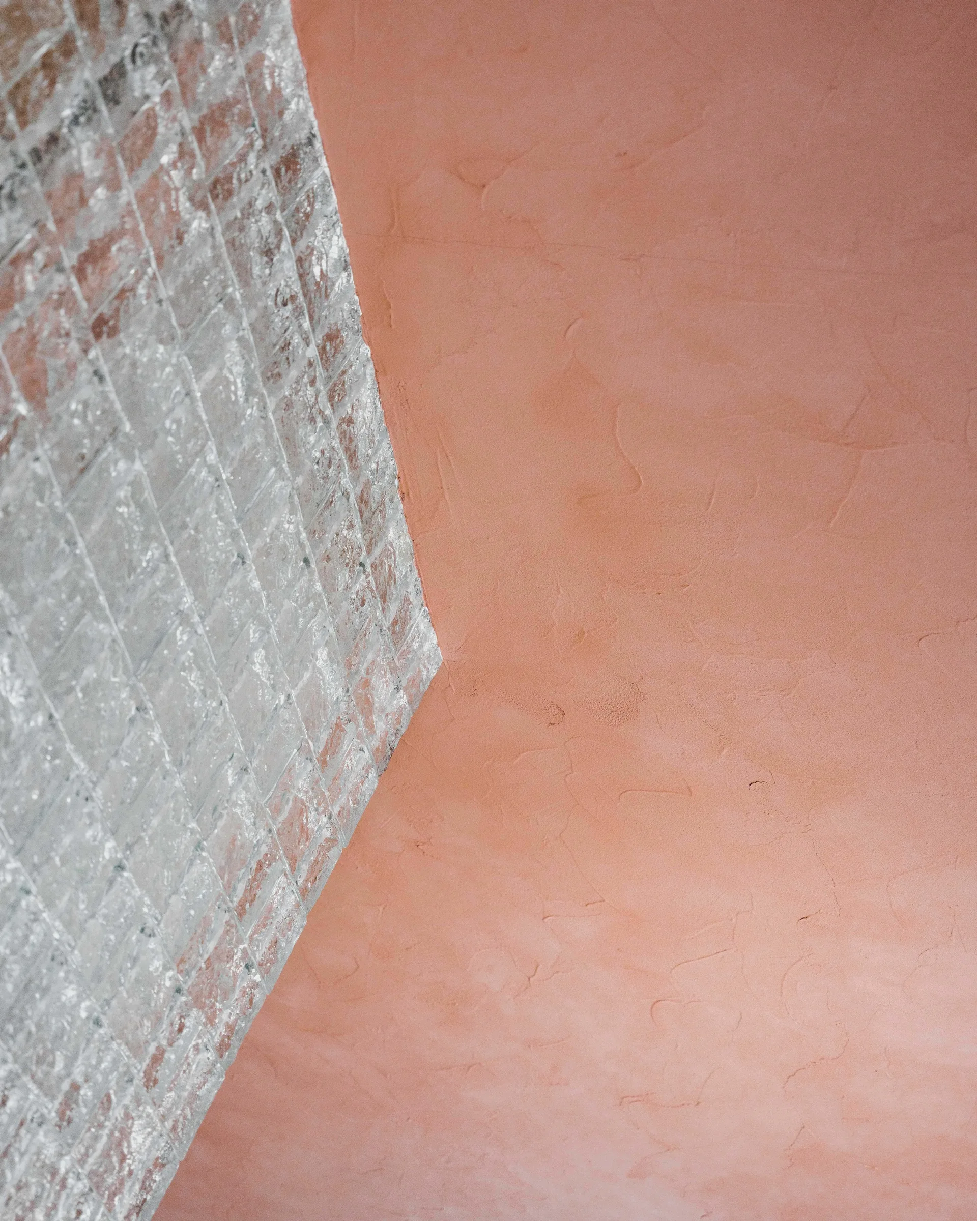 A corner detail showing a textured pink plaster wall meeting a translucent glass block partition wall.