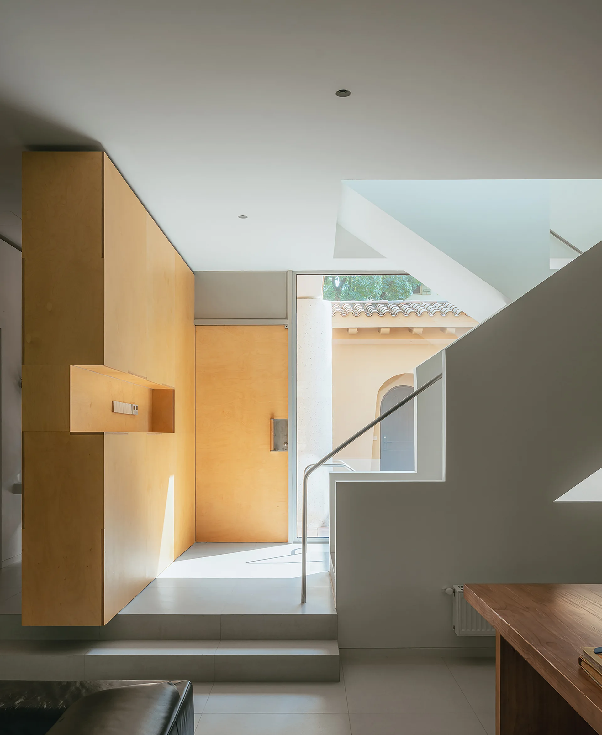 A minimalist entryway features a warm plywood accent wall with a built-in niche, a white concrete staircase, and a glass front door.
