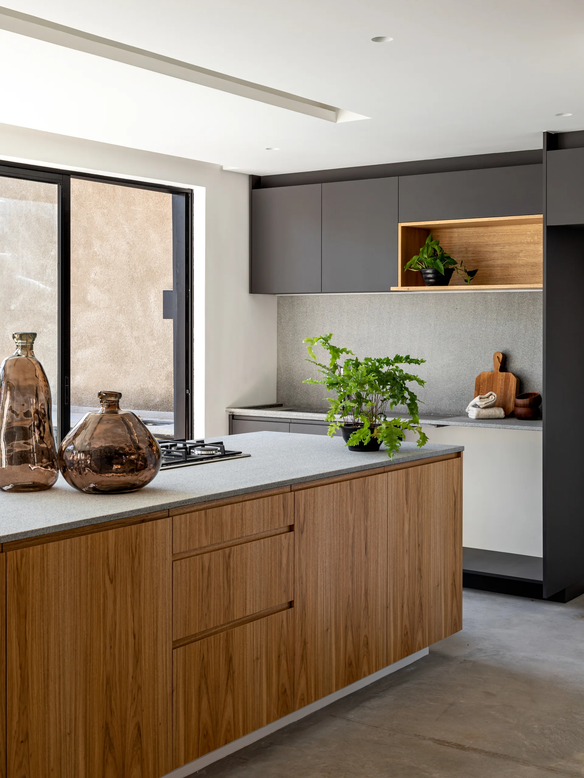 A modern kitchen featuring a wood-grained island with a grey stone countertop, dark grey upper cabinets, and a grey stone backsplash.