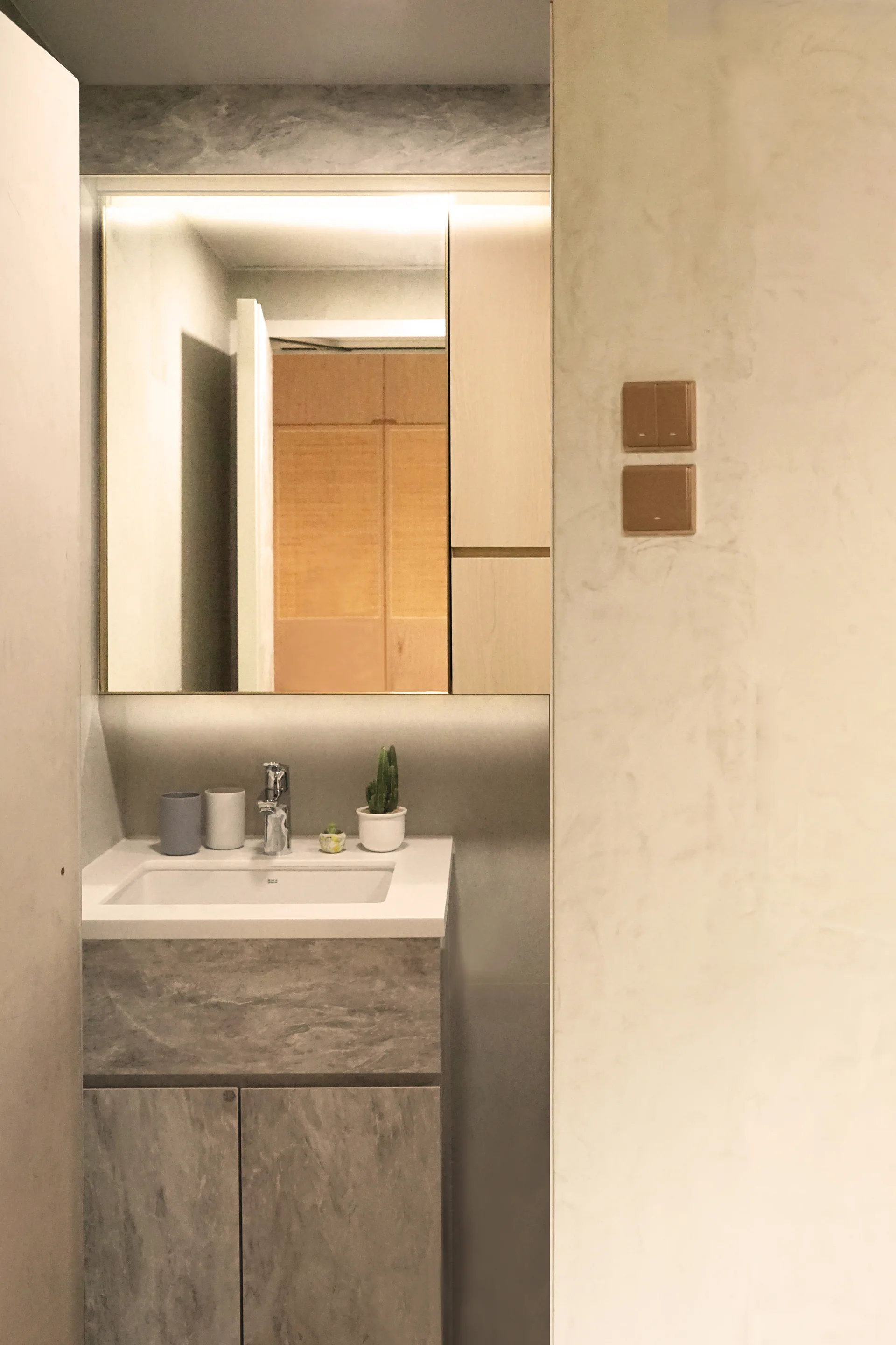 A modern grey stone-finish bathroom vanity sink is paired with a rectangular backlit mirror reflecting a wood door.