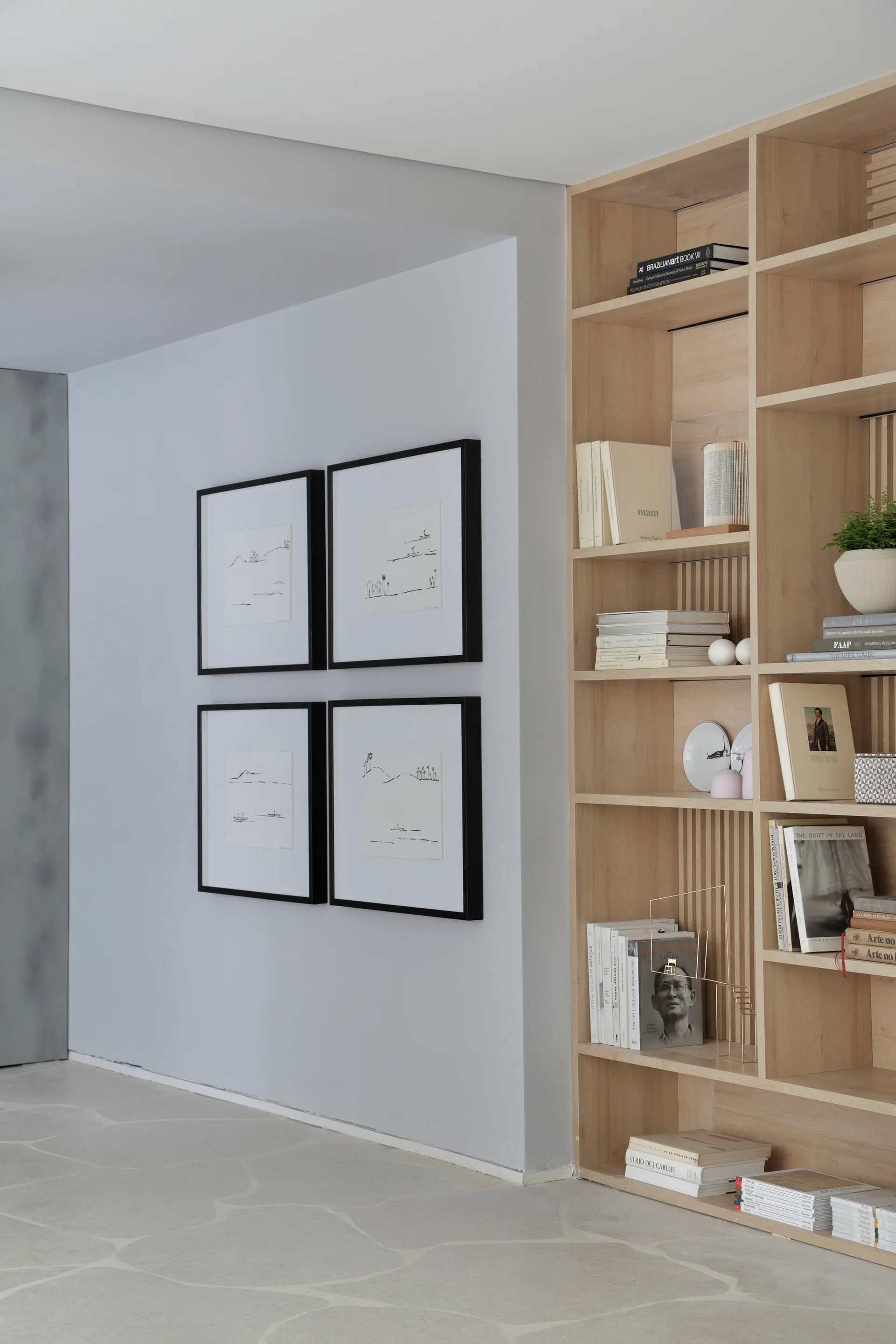 A built-in light wood bookcase filled with books and decor stands next to a light gray wall decorated with four matching black-framed sketches.