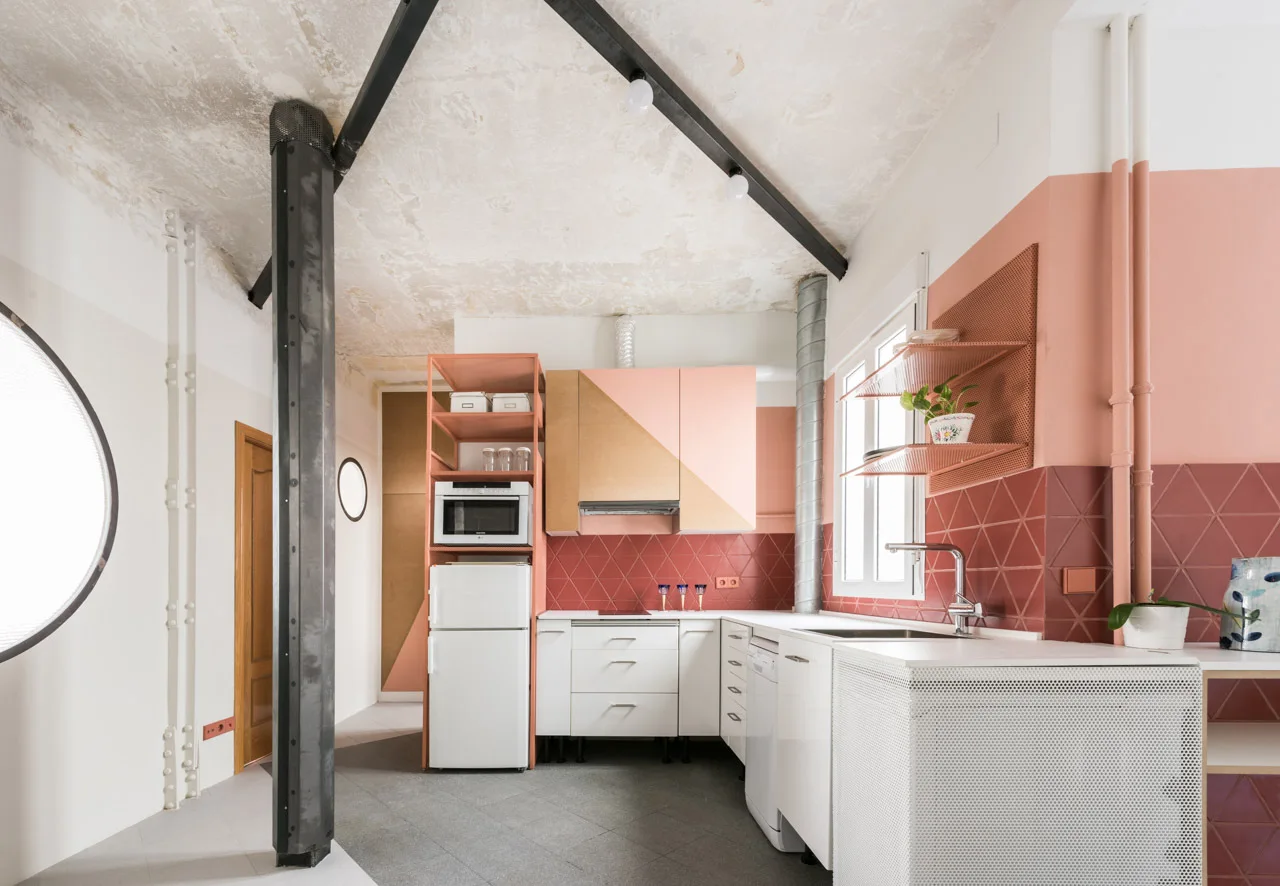 A modern kitchen with pink and beige cabinetry, a dark red geometric tile backsplash, and a prominent grey structural column.