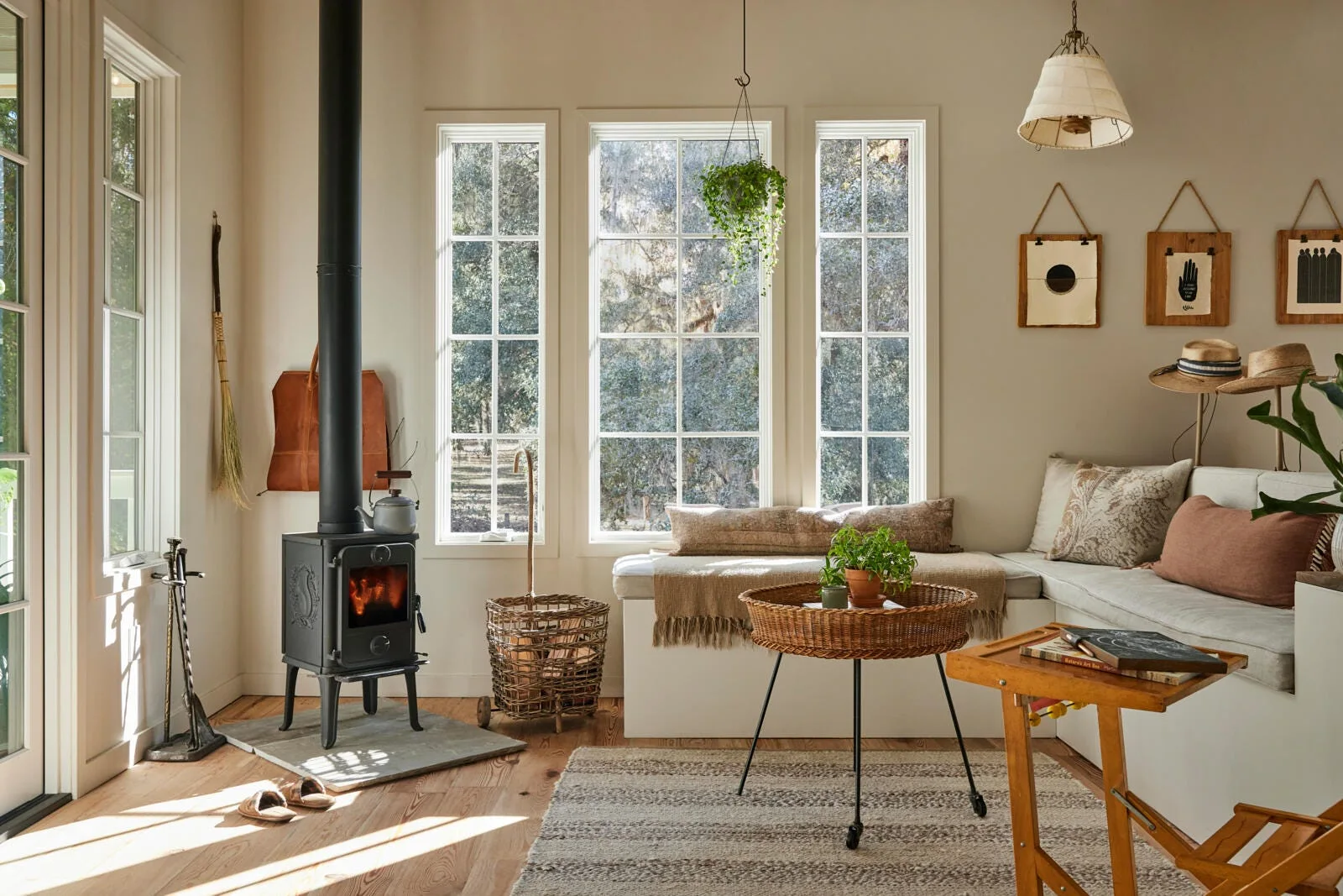 A rustic living room features a black cast-iron wood stove beside a built-in corner window seat with neutral cushions and a striped woven rug.