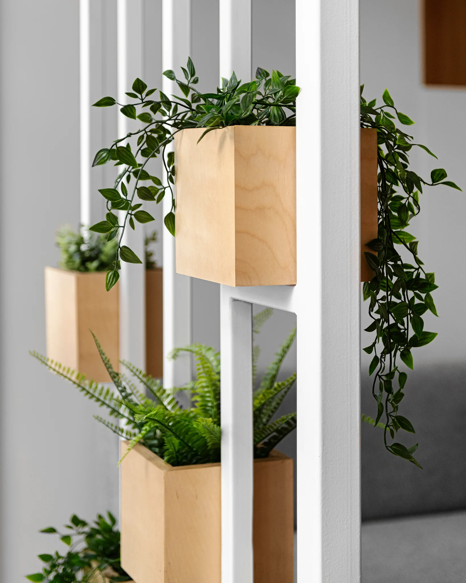 A modern white metal room divider featuring integrated square wooden planter boxes filled with cascading green plants.