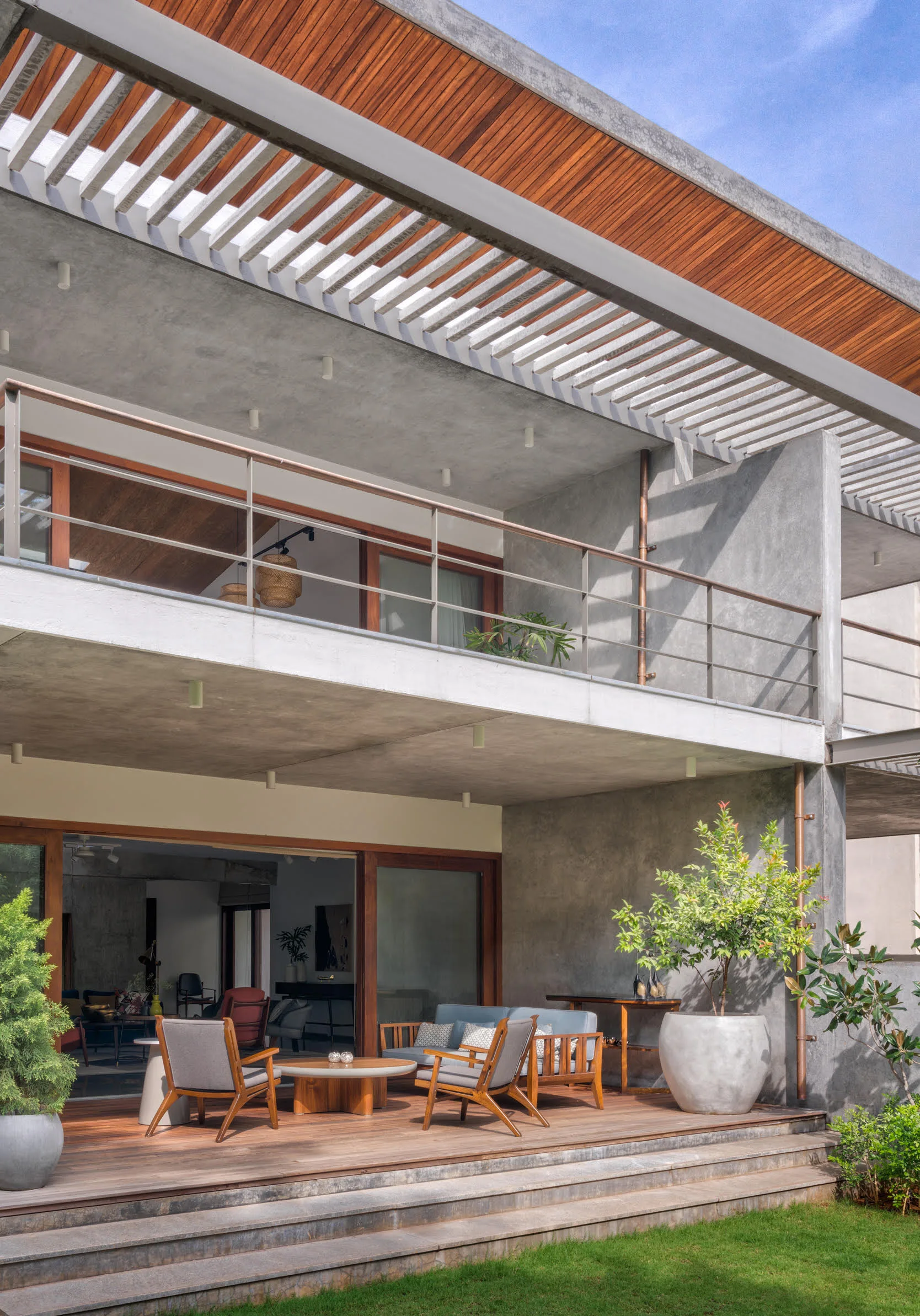 A modern concrete patio features a wood deck with armchairs and a coffee table beneath a slatted wooden ceiling.