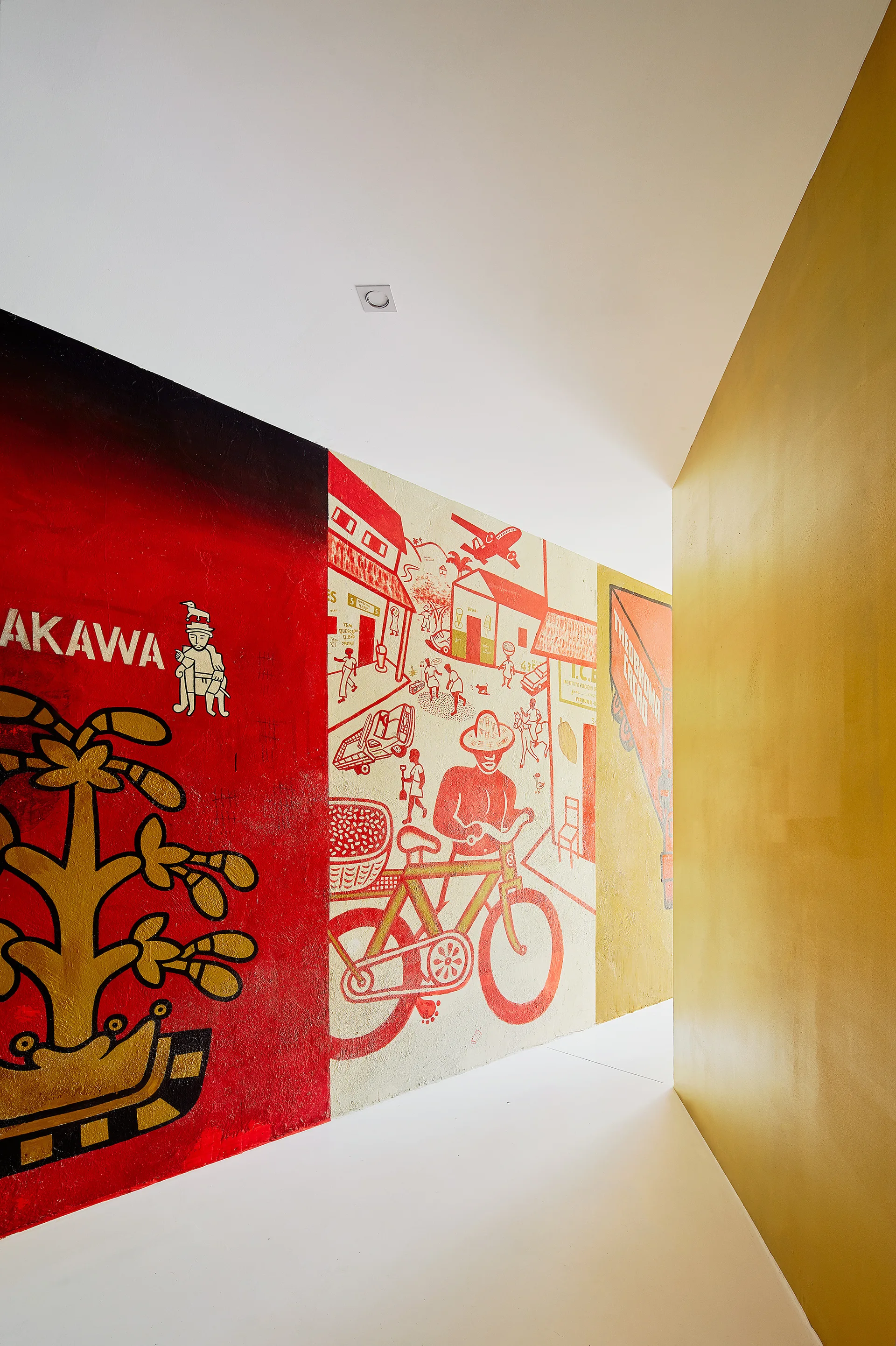 A modern corner wall features a detailed red and gold illustrated mural next to a solid gold painted wall under a white ceiling.