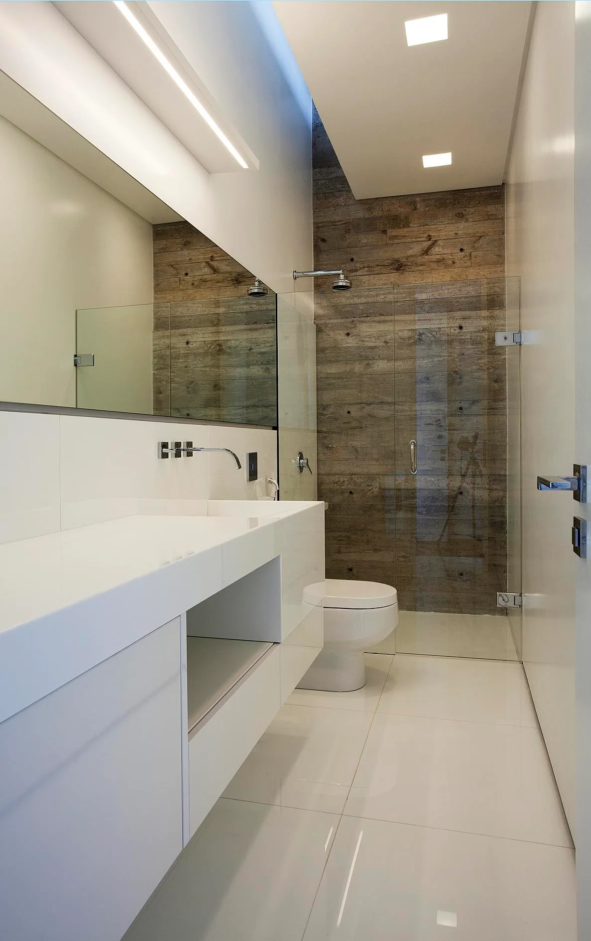 A modern bathroom features a glossy white floating vanity, a large wall mirror, and a glass-enclosed shower with a wood-grain textured wall.