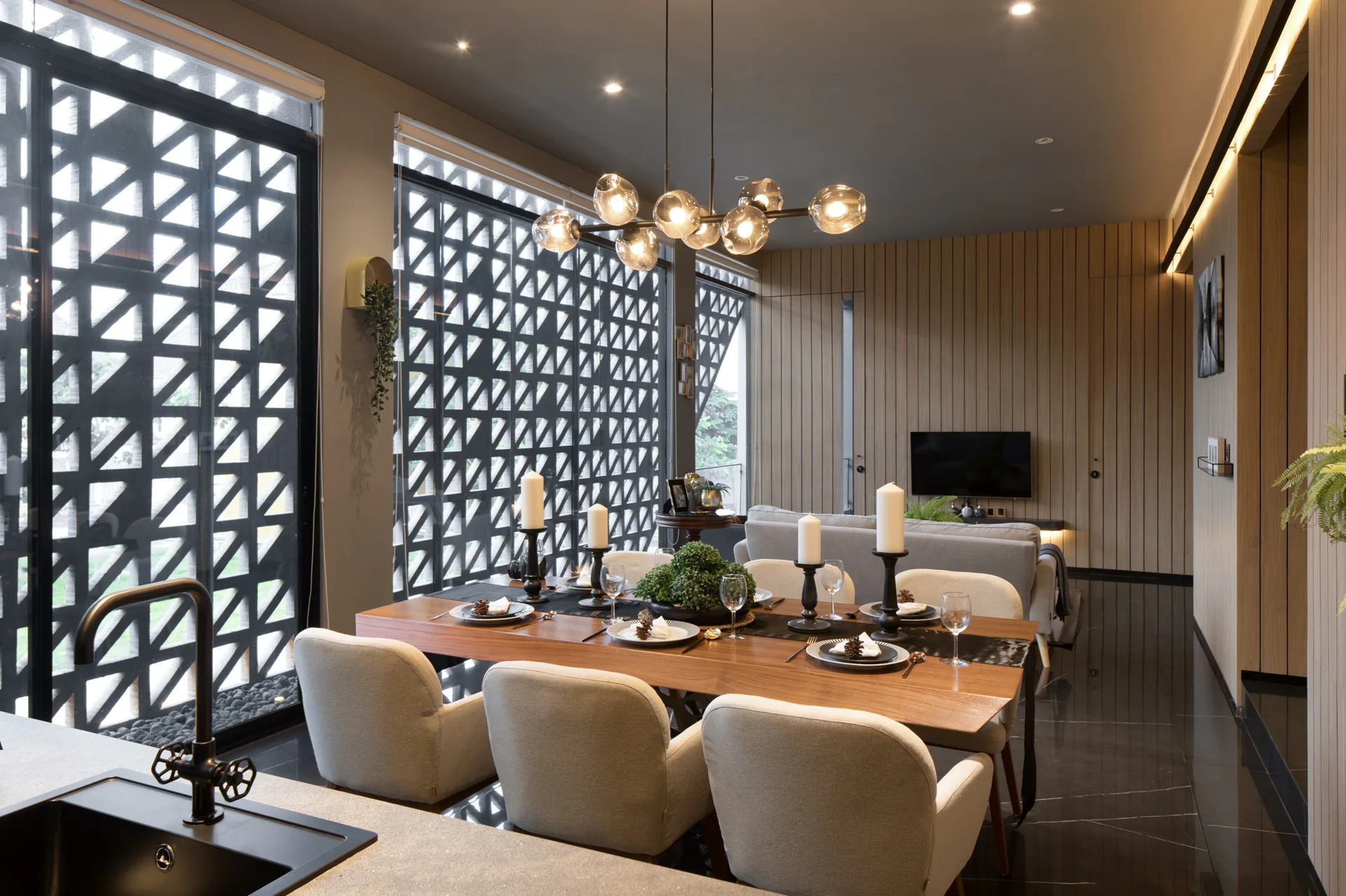 A modern dining room features a wood table with cream chairs under a multi-globe chandelier, set against a black geometric screen and slatted wood wall.
