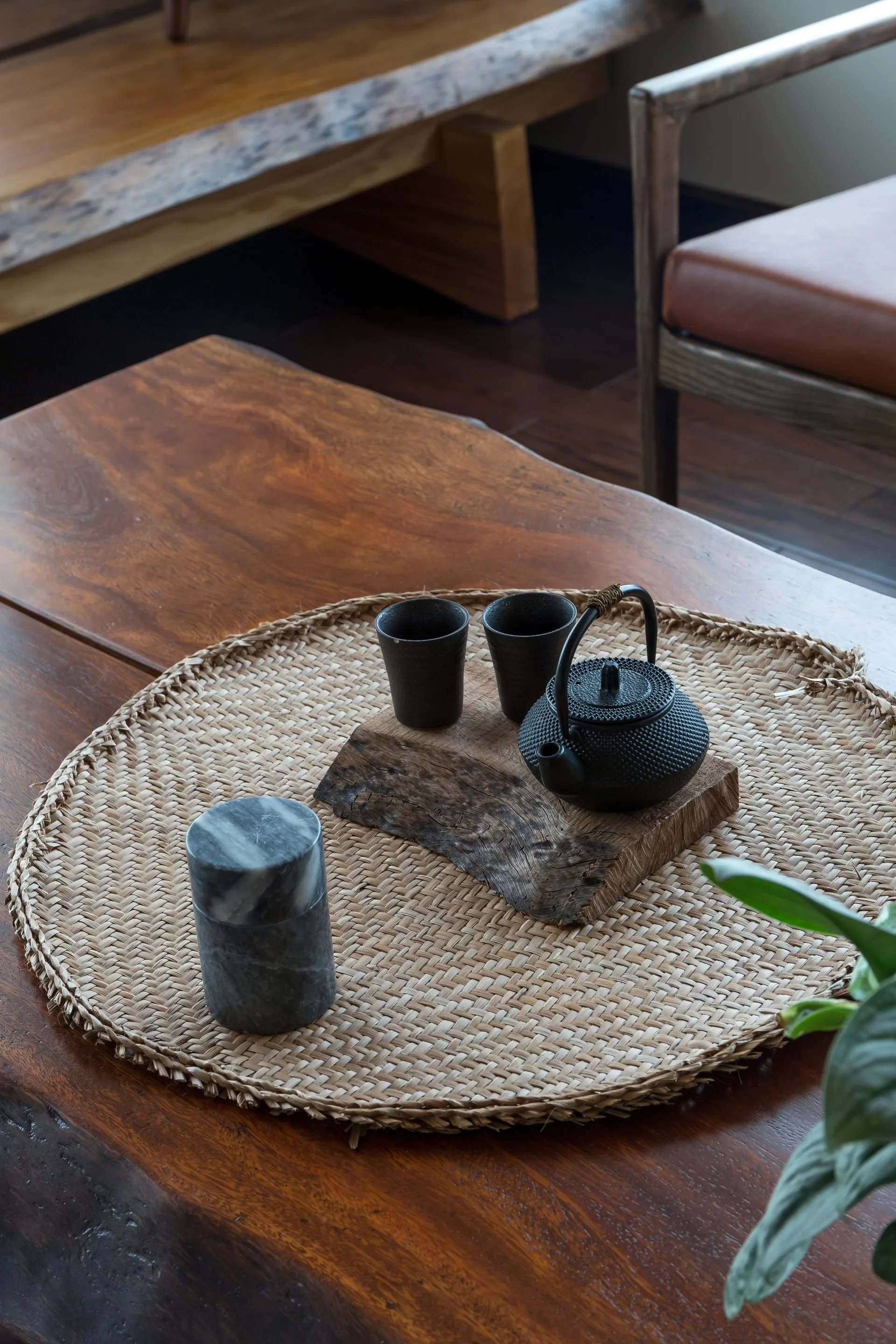A cast iron tea set rests on a rustic wood slice and circular woven placemat on a dark wooden coffee table.
