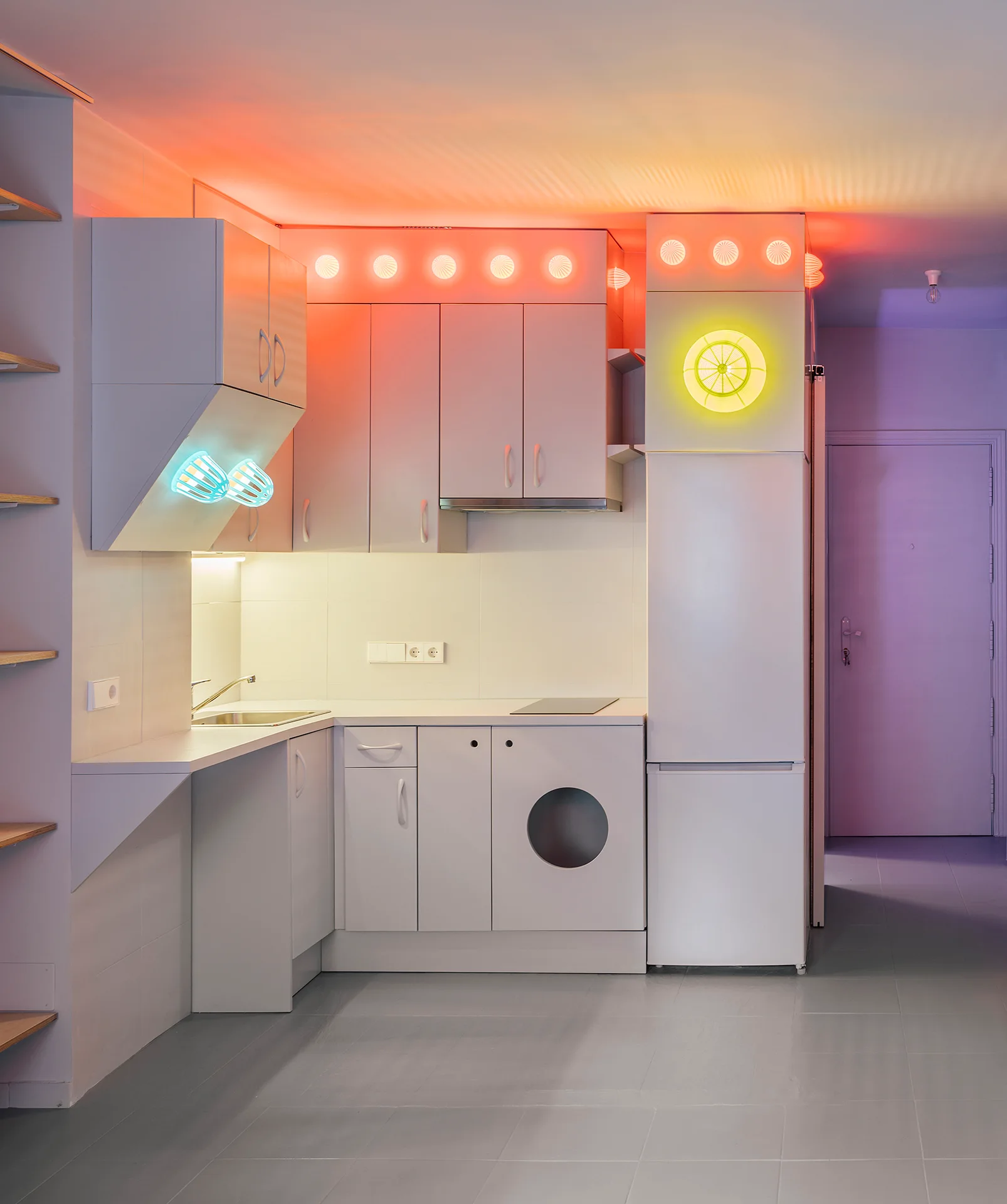 A minimalist white kitchen featuring flat-panel cabinets, integrated appliances, and vibrant neon blue, orange, and yellow accent lighting.