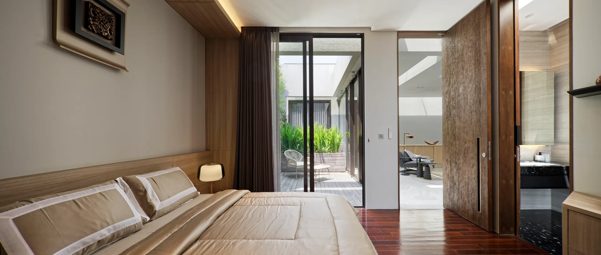 A modern bedroom features beige bedding, built-in wood wall paneling, and sliding glass doors that open to an outdoor patio with a chair.