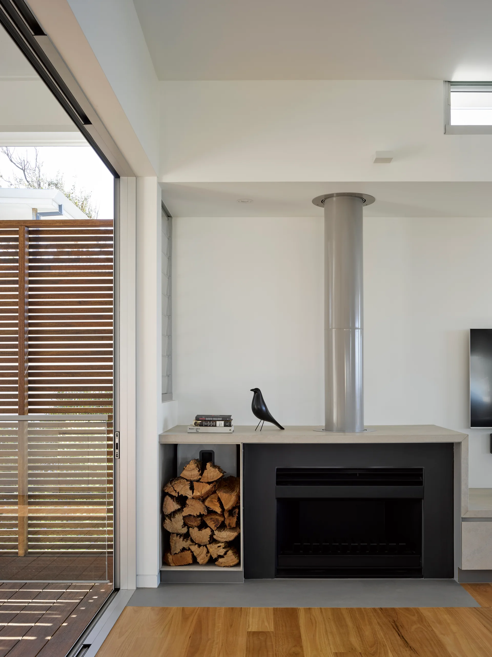 A modern black fireplace with a grey cylindrical flue features an integrated firewood niche next to a large sliding glass door.
