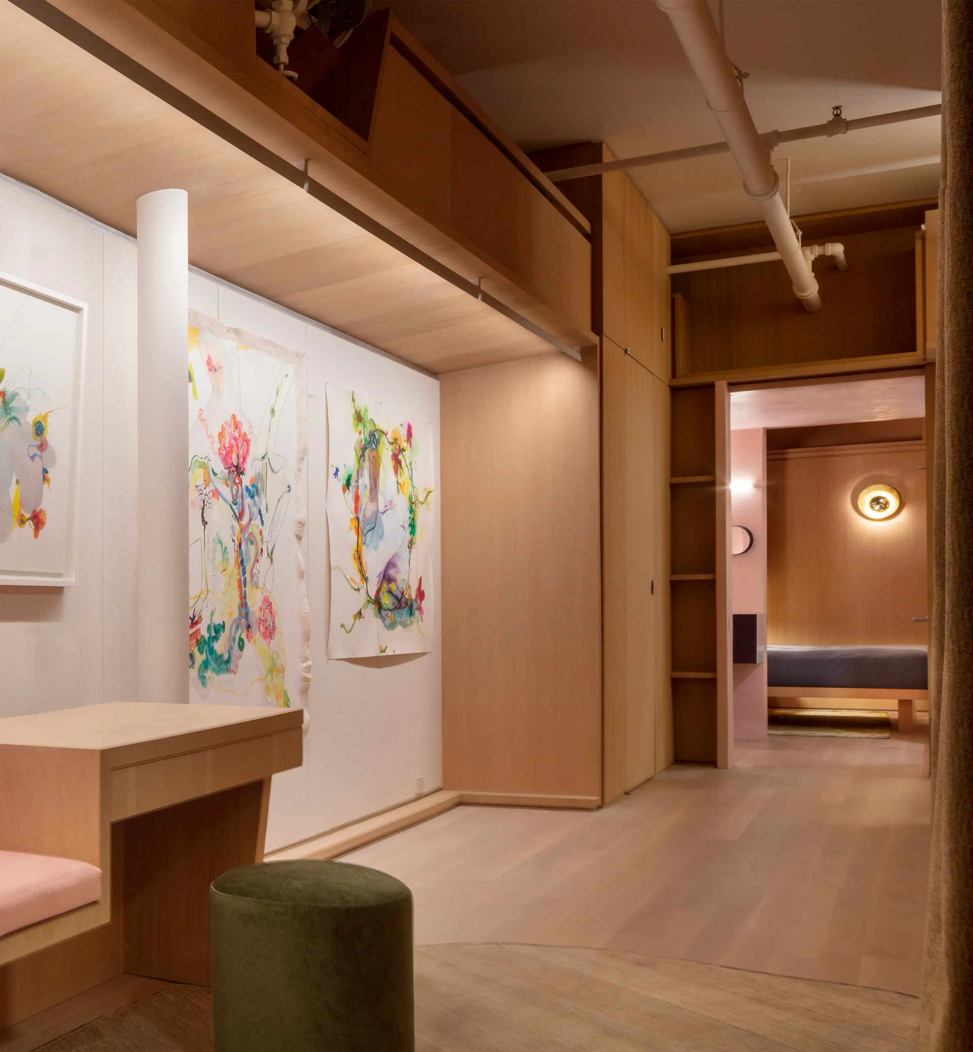 A modern hallway featuring light wood built-in cabinetry, an integrated desk with a green stool, and abstract colorful artwork on the wall.