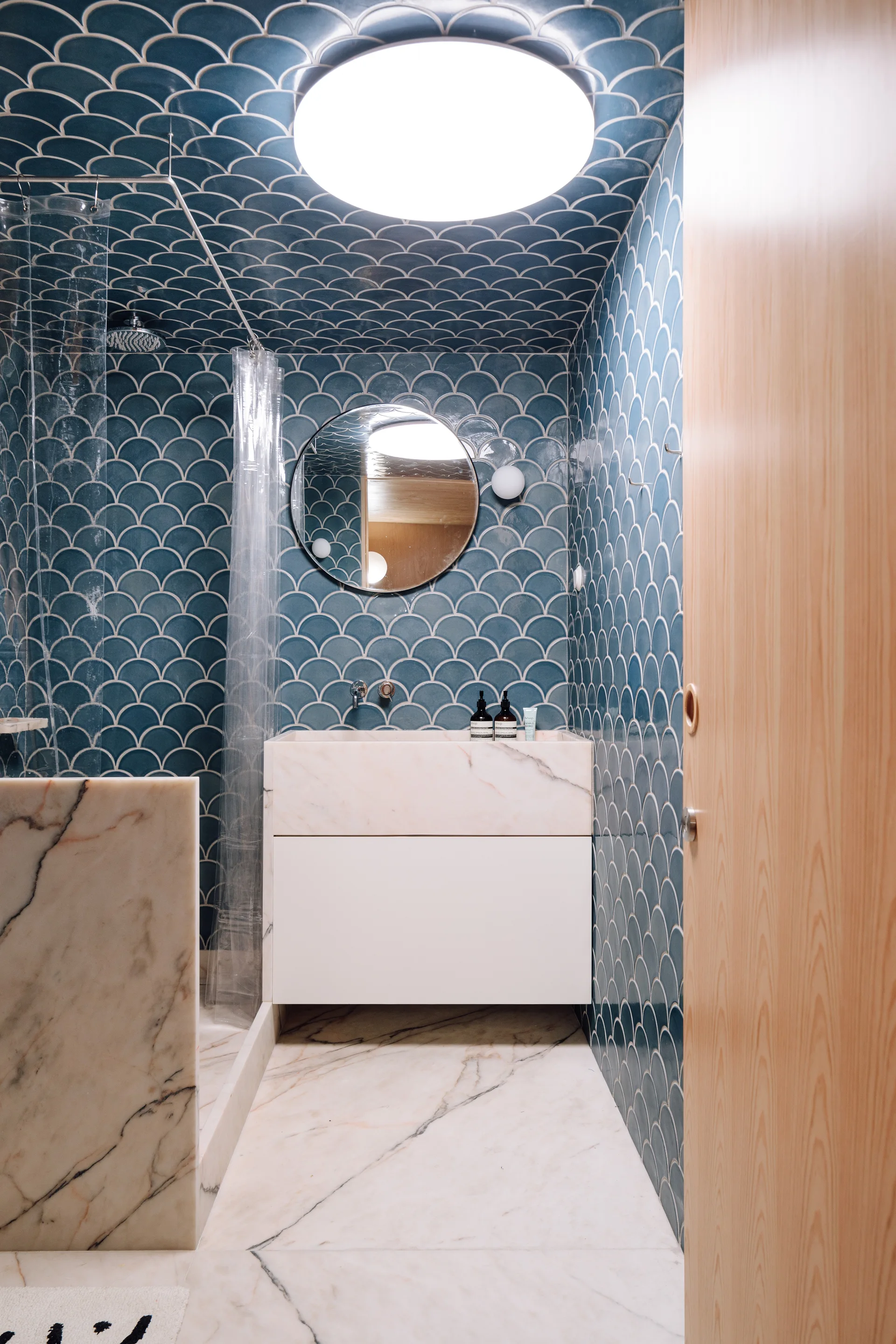 A modern bathroom features blue scallop-patterned tiles on the walls and ceiling, a white floating marble vanity, and marble flooring.