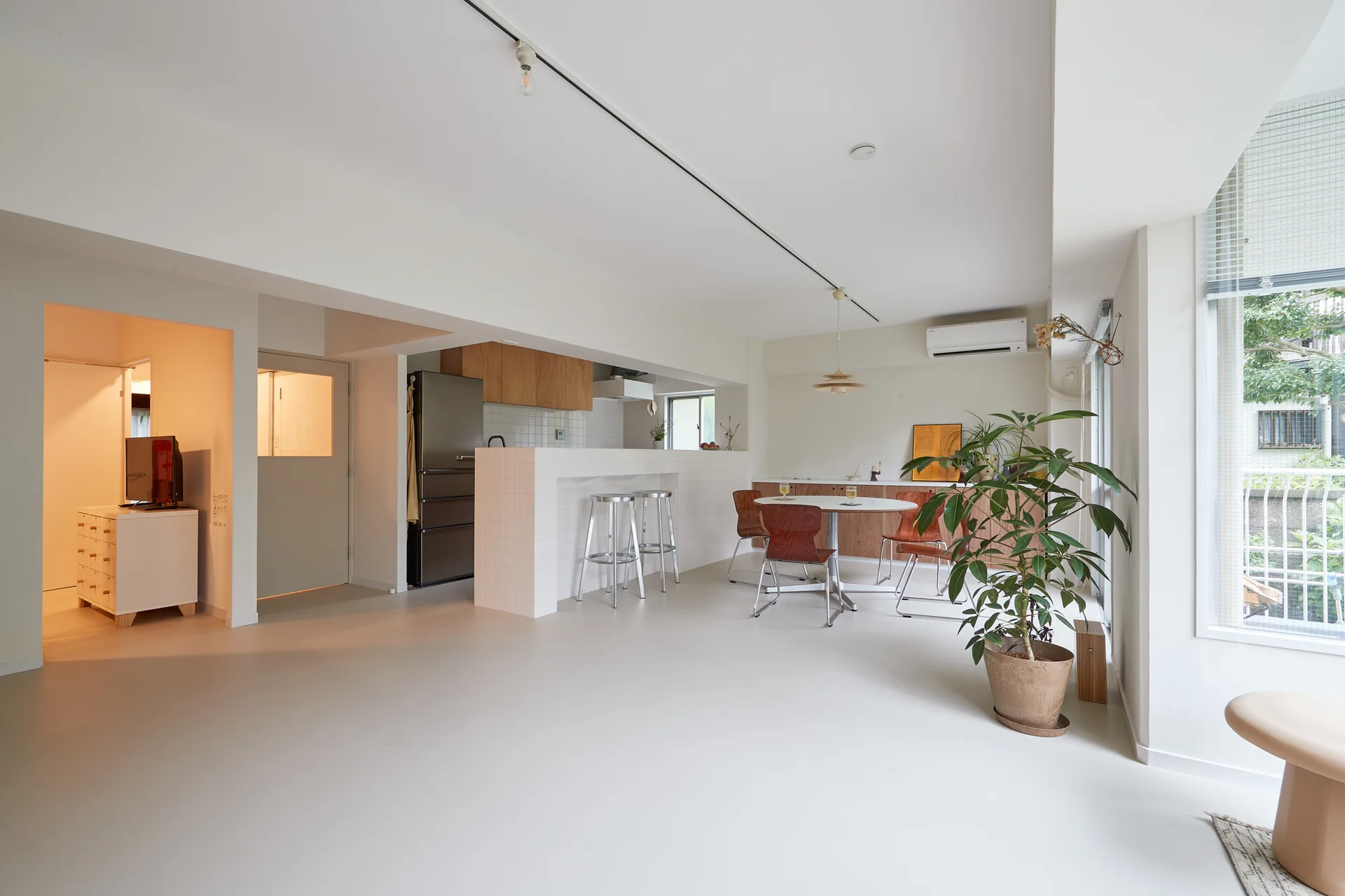 An open-concept minimalist dining and kitchen area features a white tiled island, wooden chairs around a round table, and a large potted plant.