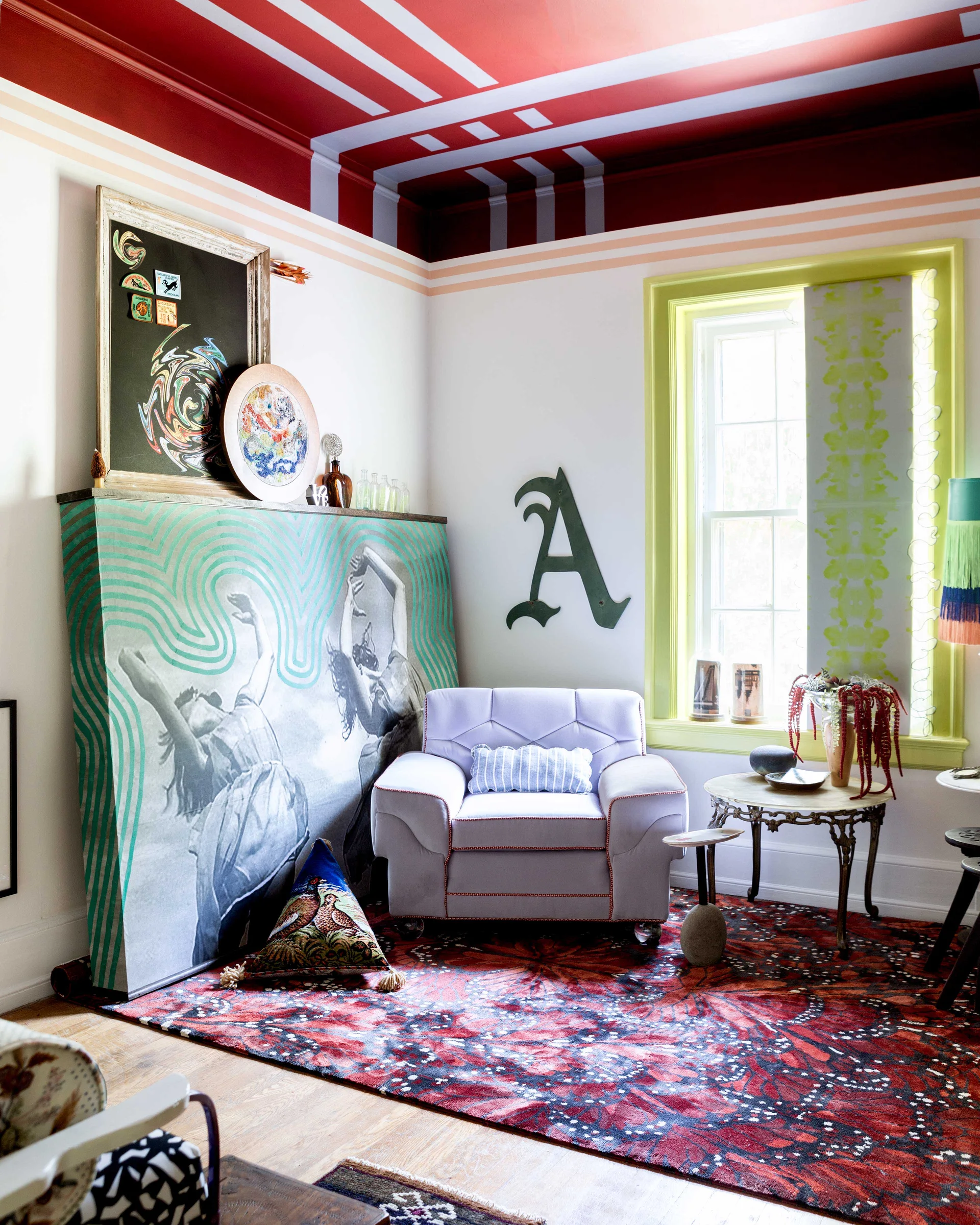 A light purple armchair sits on a red patterned rug beneath a striped red ceiling in an eclectic living room next to a lime green window.