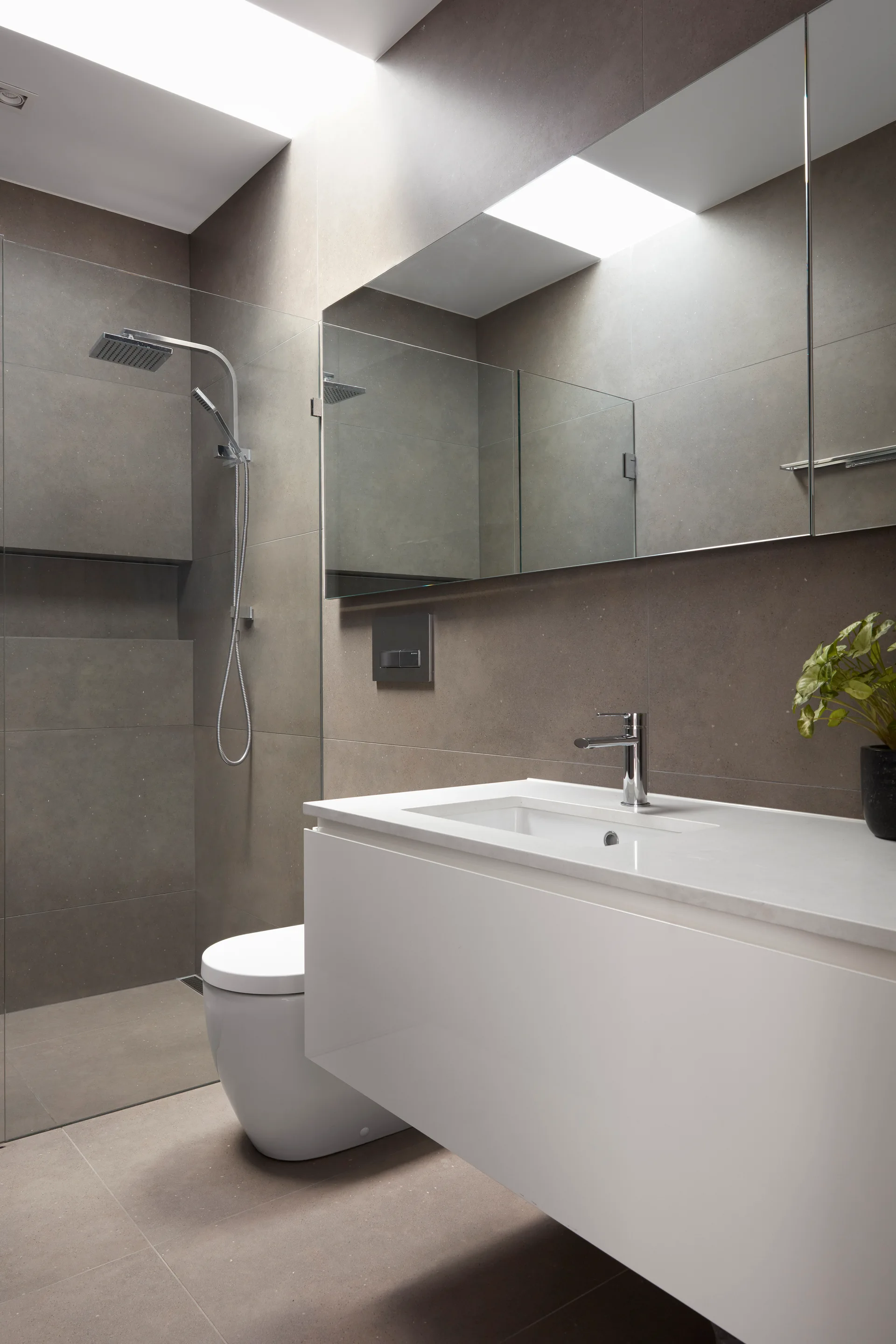 A minimalist bathroom featuring matte gray wall and floor tiles, a white floating vanity with a chrome faucet, and a skylight filtering natural light.