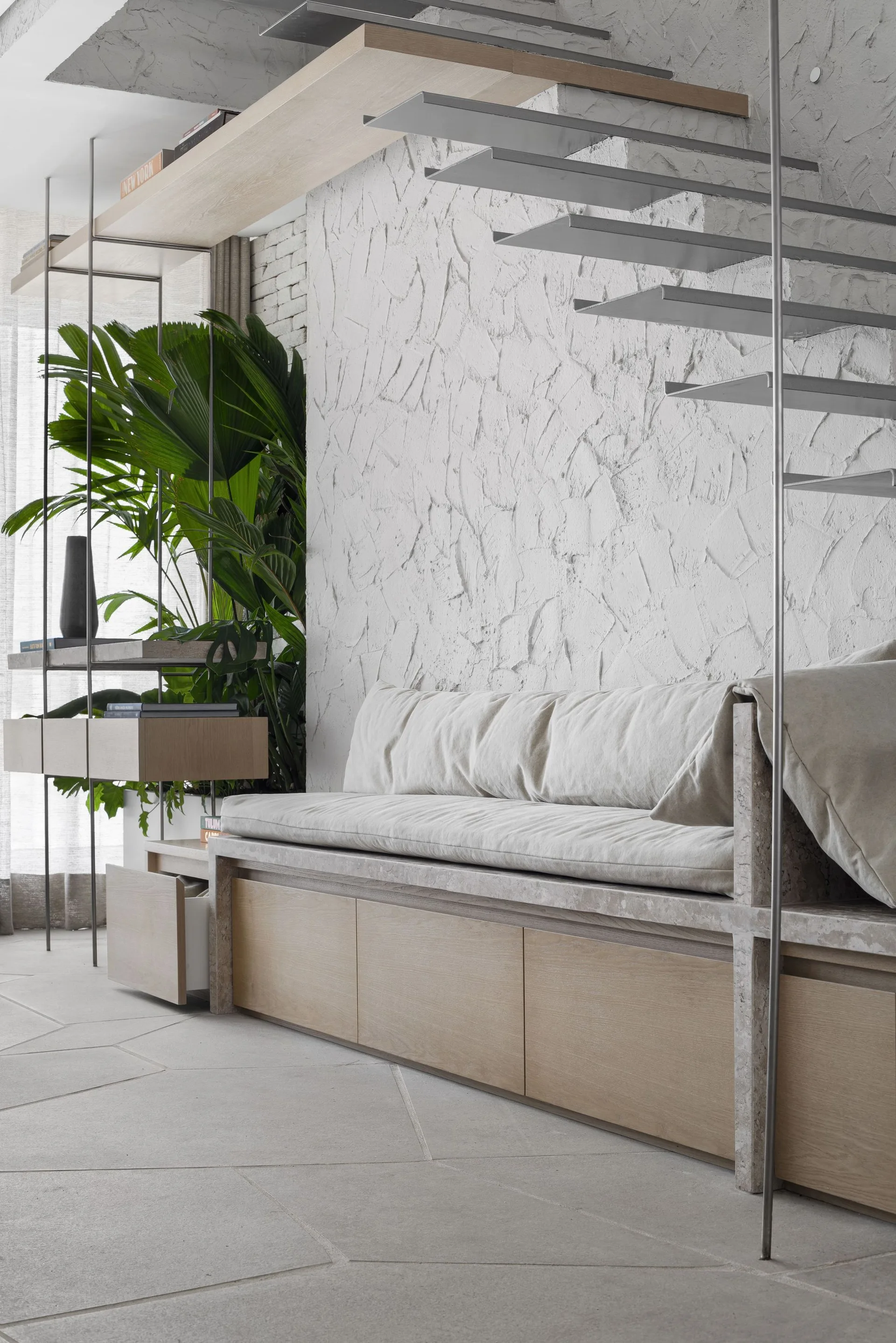 A custom wooden bench with a beige cushion sits beneath open-tread metal stairs against a heavily textured white plaster wall.