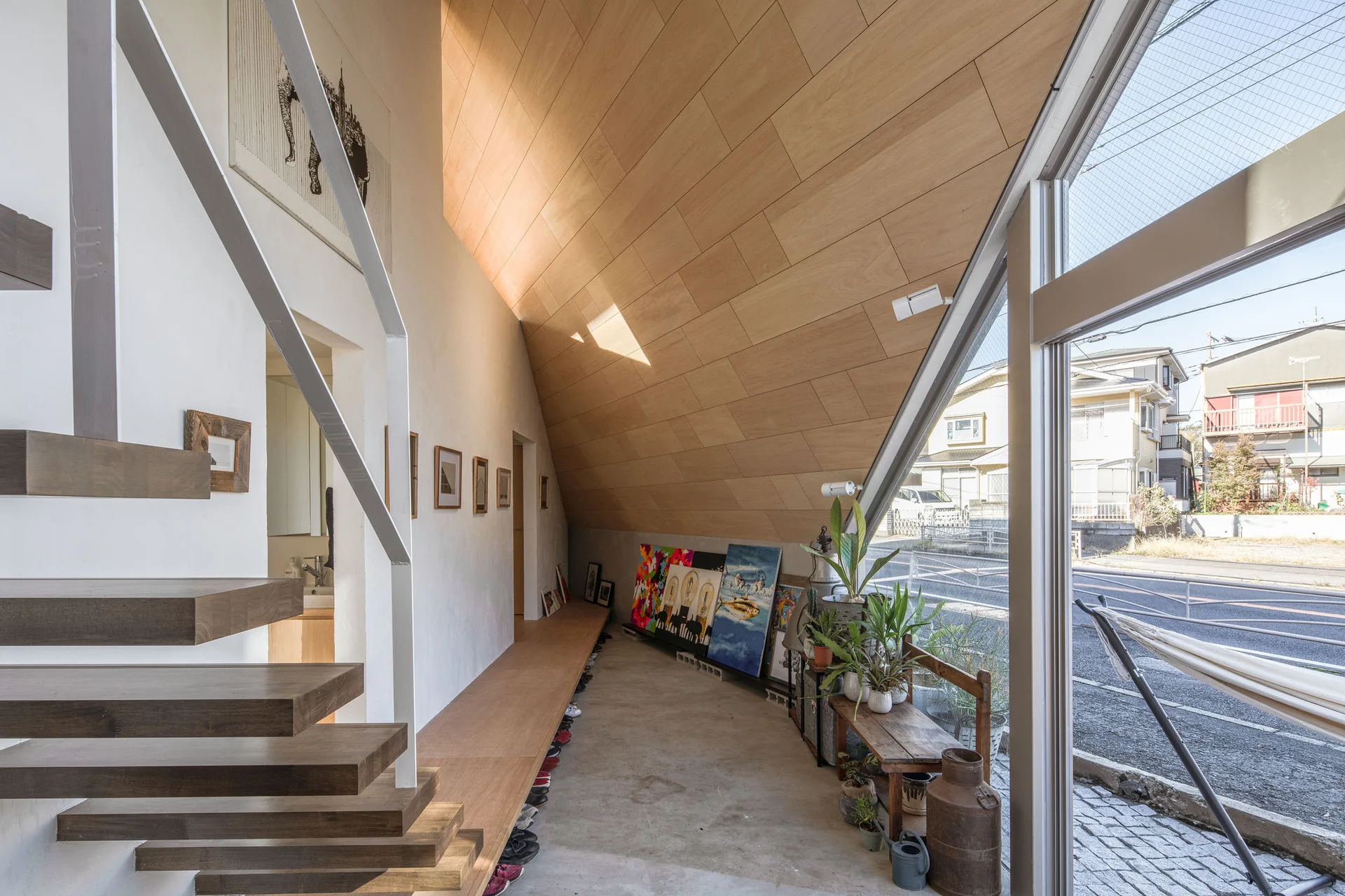 A minimalist entryway featuring a sloped light wood paneled ceiling, a cantilevered staircase, and concrete flooring with large glass windows.