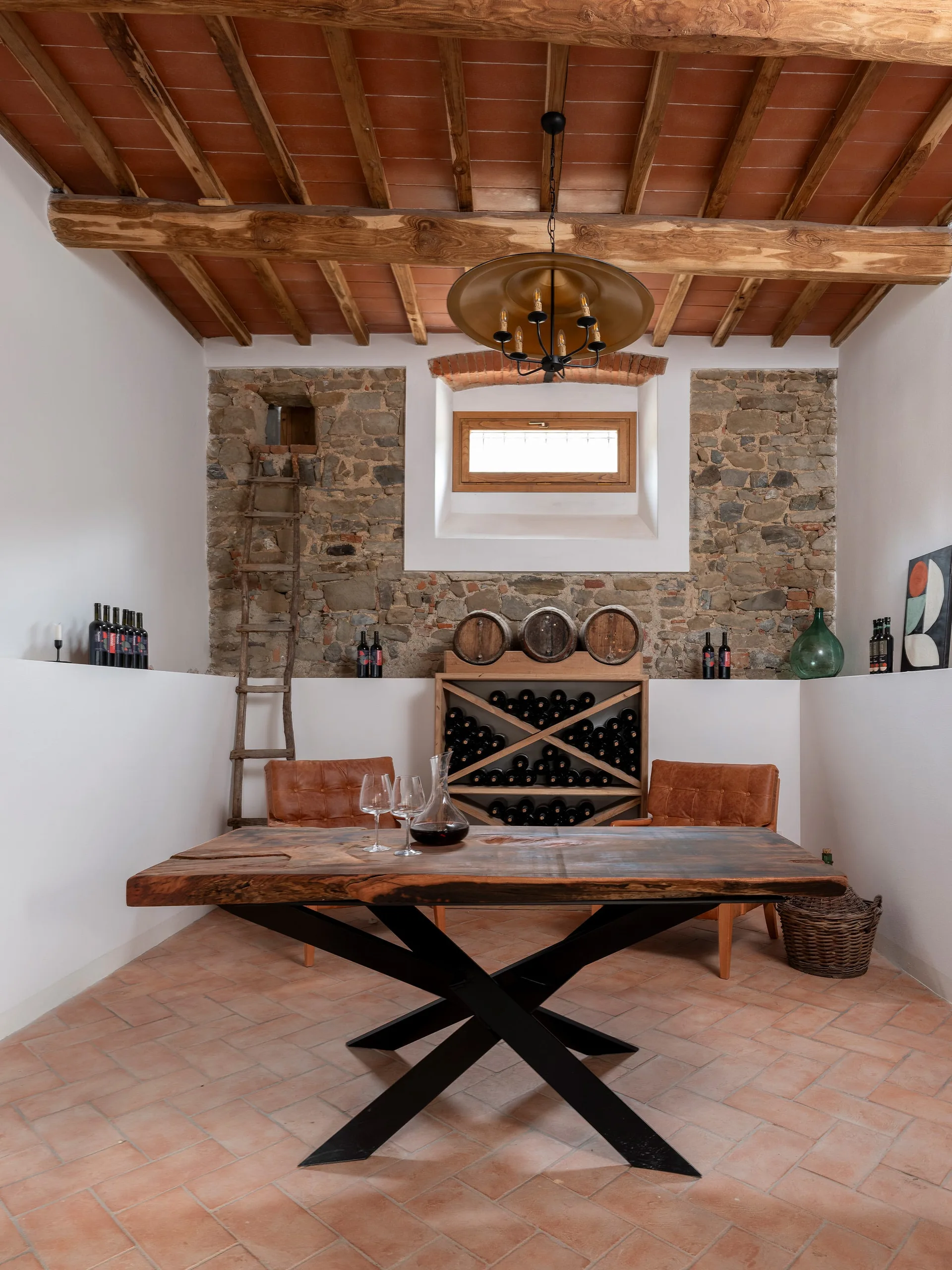 A rustic wine tasting room features a live-edge wooden table, leather armchairs, an exposed stone accent wall, and wood-beamed ceilings.