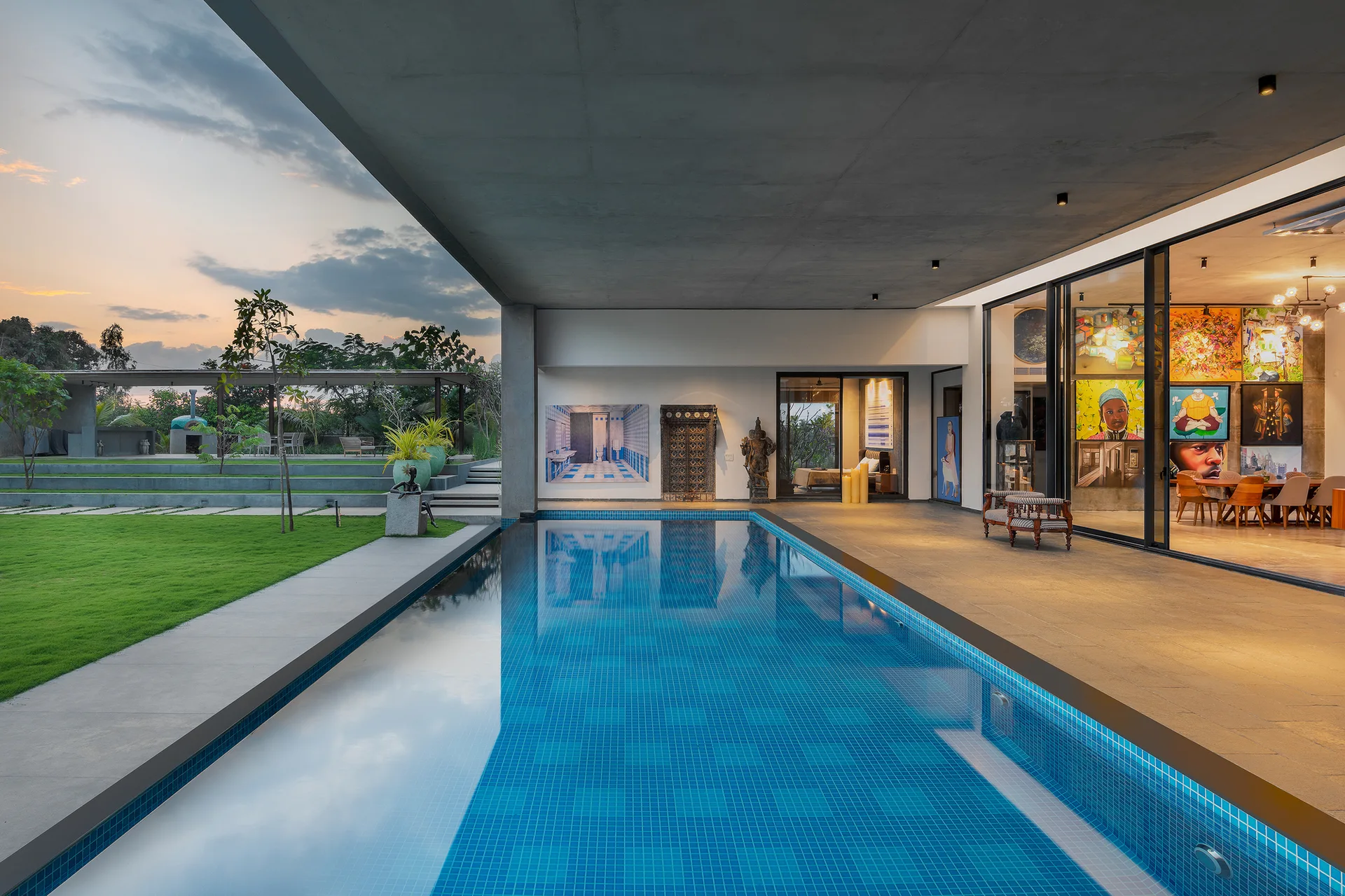 A modern outdoor swimming pool with blue tiles next to a covered concrete patio and large sliding glass doors.