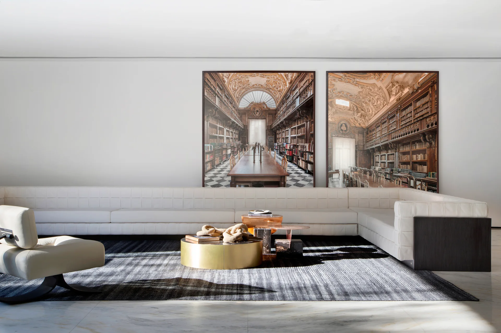 A minimalist living room features an extra-long white tufted sectional sofa, a round gold coffee table, and two large architectural prints on the wall.