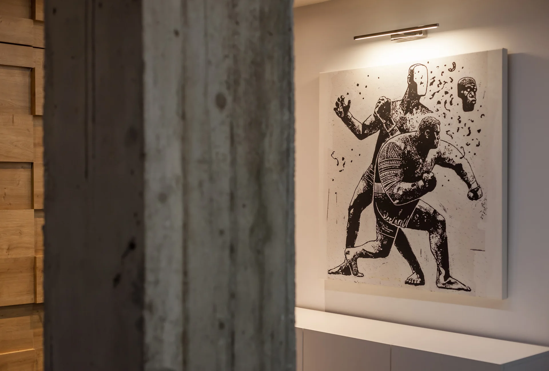 A large black and white graphic artwork hangs on a white wall above a low console, next to a textured concrete column and wood paneling.