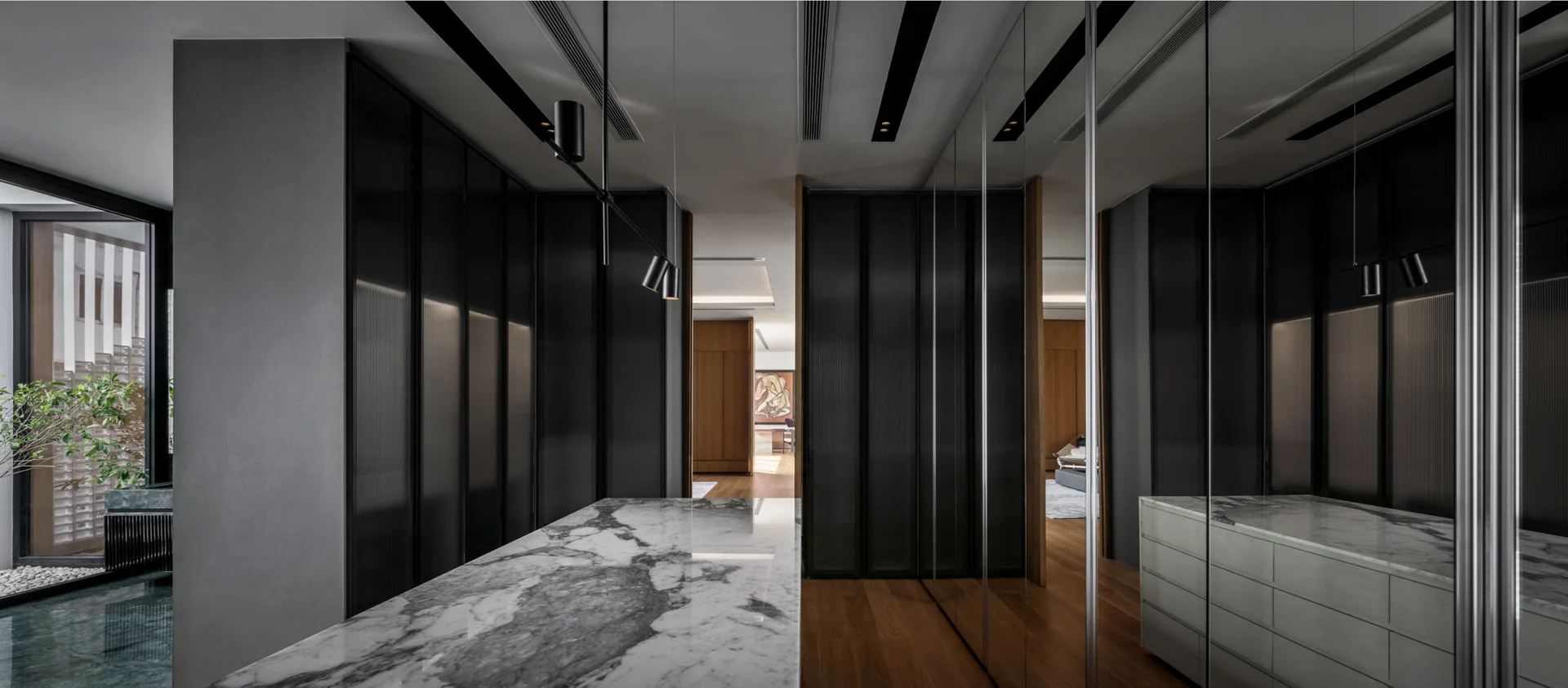 A minimalist dressing room featuring a marble-topped island, dark fluted glass wardrobes, and a wall of mirrored panels.