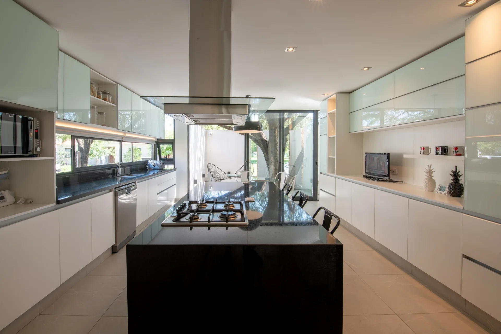 A modern kitchen with a long black granite island, white lower cabinetry, and reflective glass-front upper cabinets.