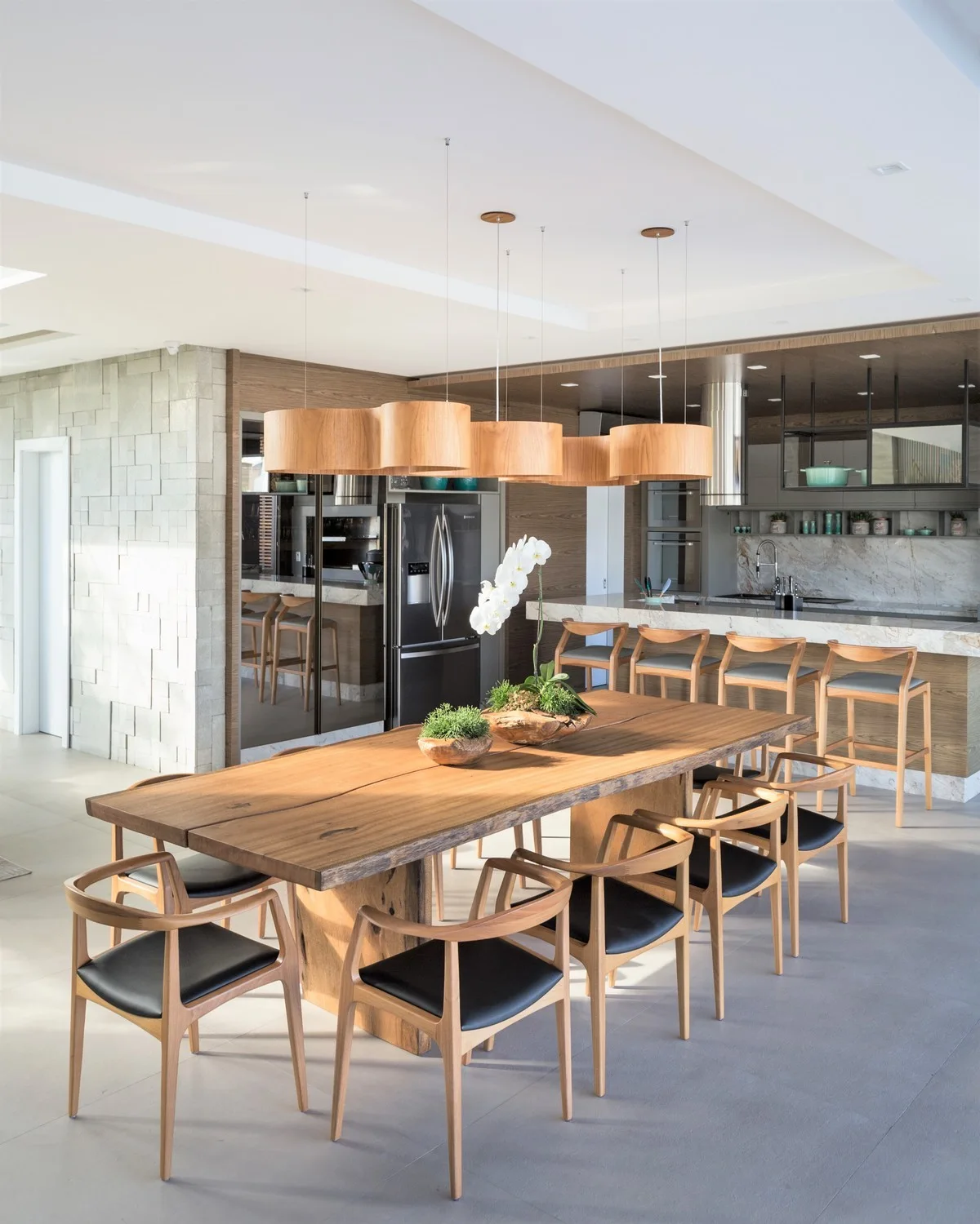 An open-concept dining area features a live-edge wood table with black-cushioned chairs beneath a row of cylindrical wooden pendant lights.