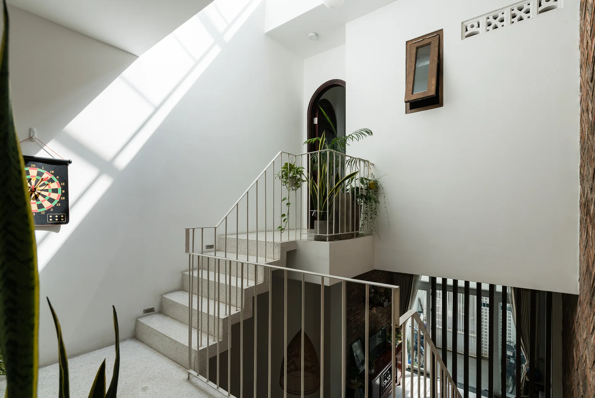 A white staircase with speckled terrazzo steps and a slim metal railing is illuminated by direct sunlight from an overhead skylight.