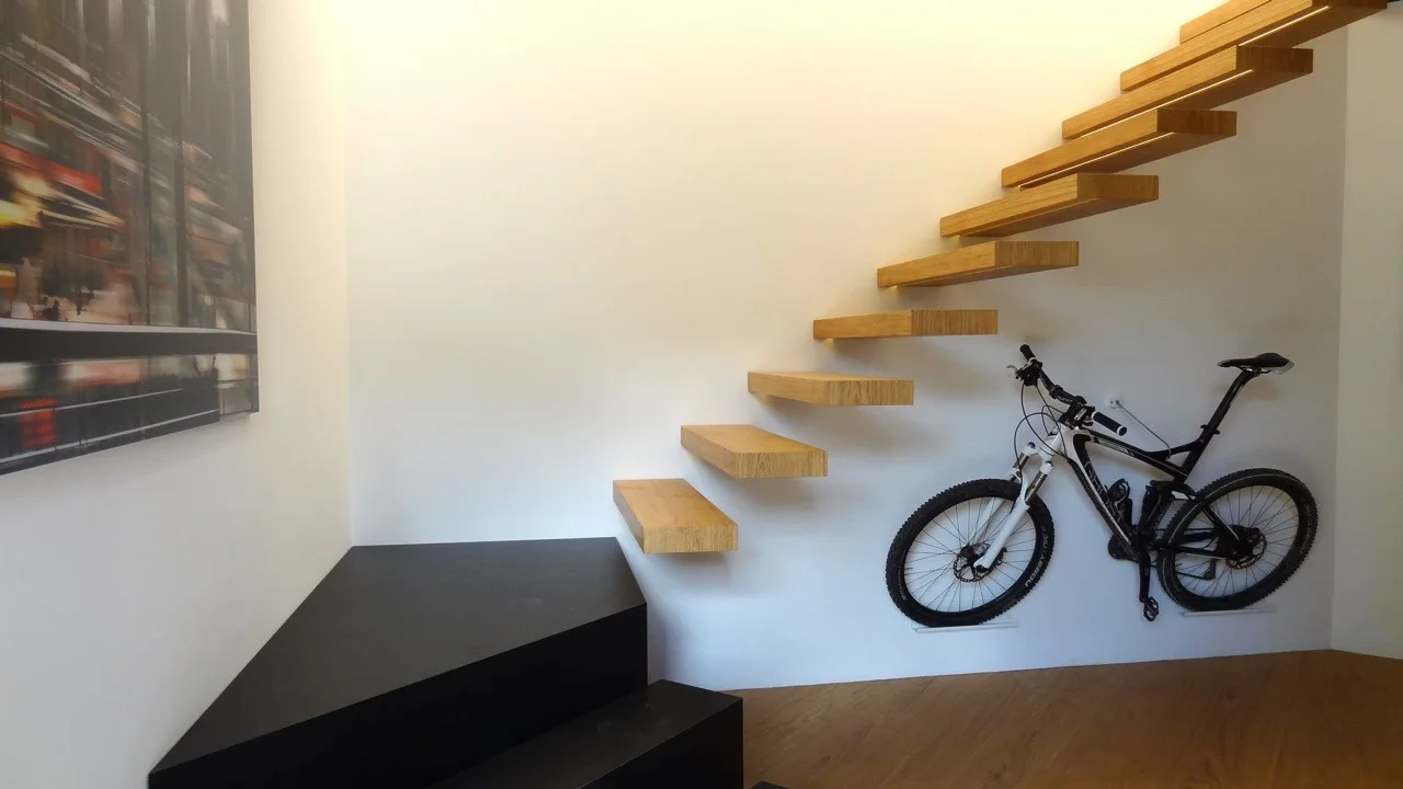 A minimalist white stairwell featuring floating wood steps above a black angular platform and a bicycle mounted directly to the wall.