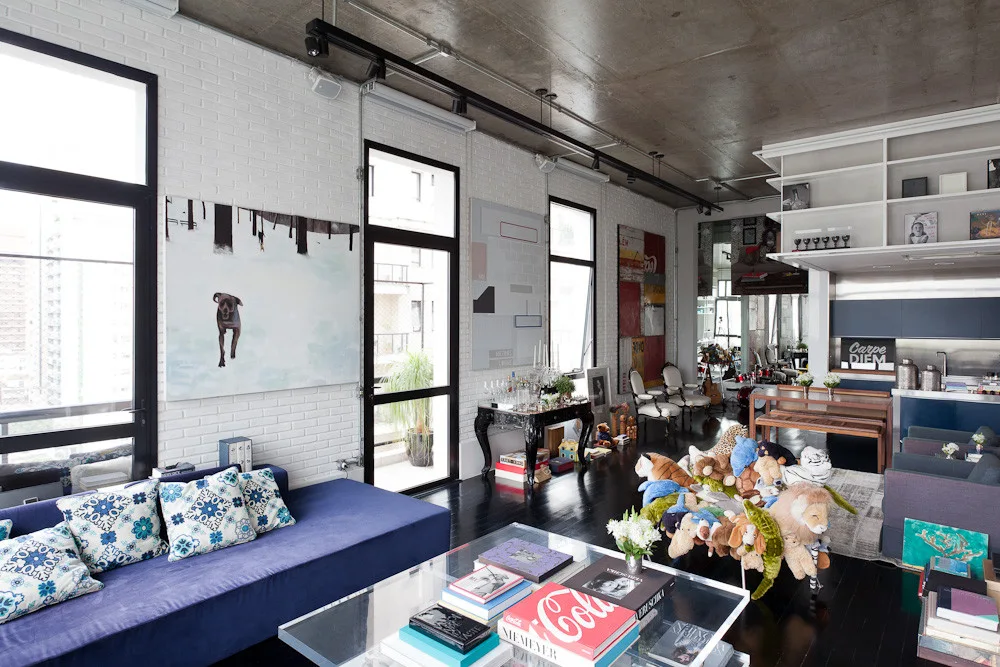 An industrial loft living room features a purple sofa, white painted brick walls, an exposed concrete ceiling, and a glass coffee table.